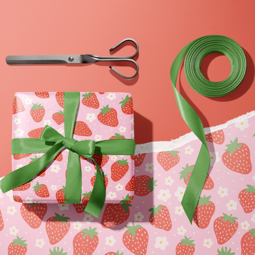 A gift wrapped present, wrapped up in bright pink and red strawberry print gift wrap from The Happy Badger.