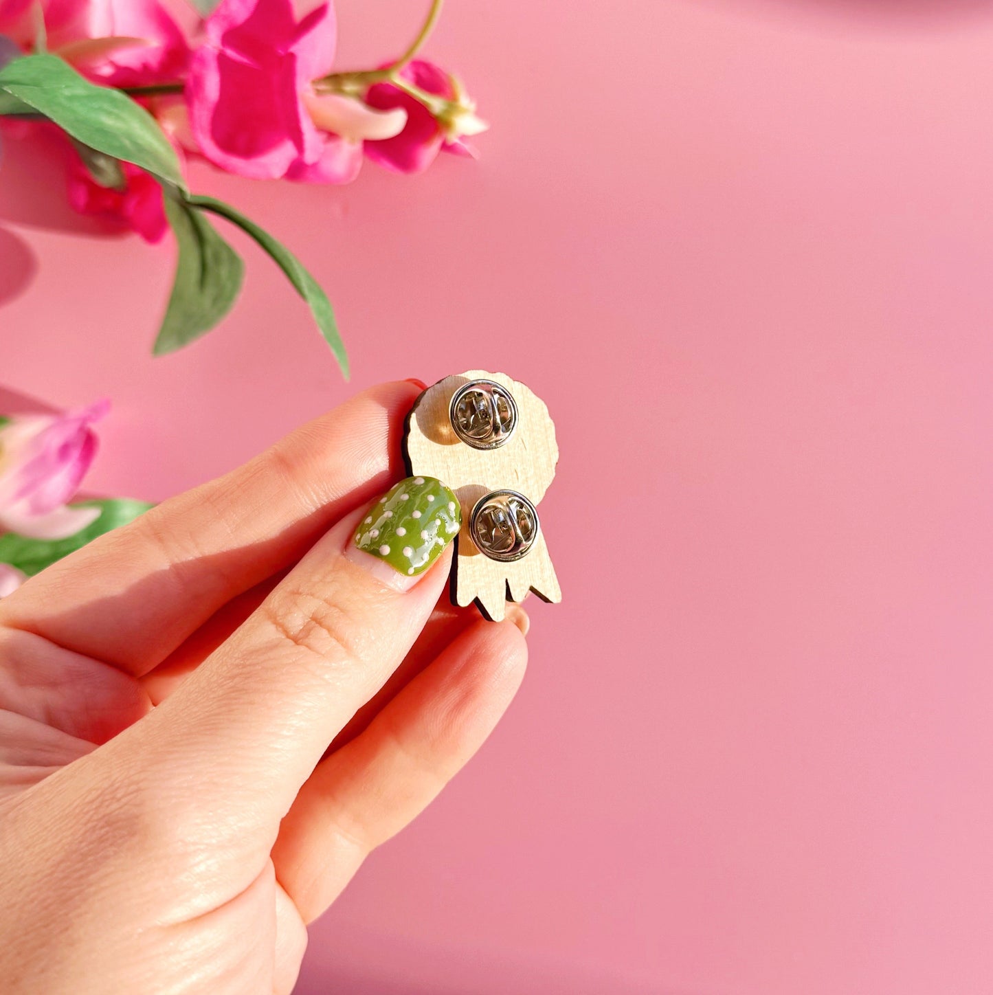 The back of a wooden pin badge with two metal clasp fastenings.