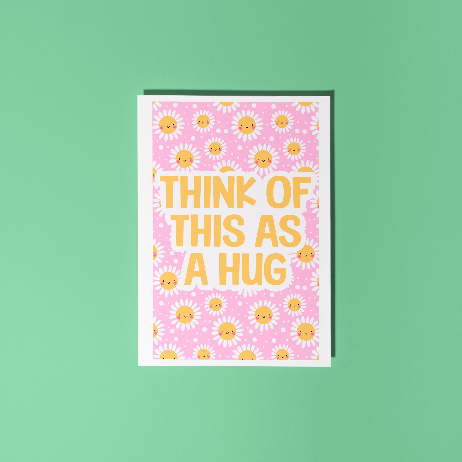 A bright pink and yellow greetings card, with a smiling daisy pattern. The text on the card reads 'think of this as a hug'.
