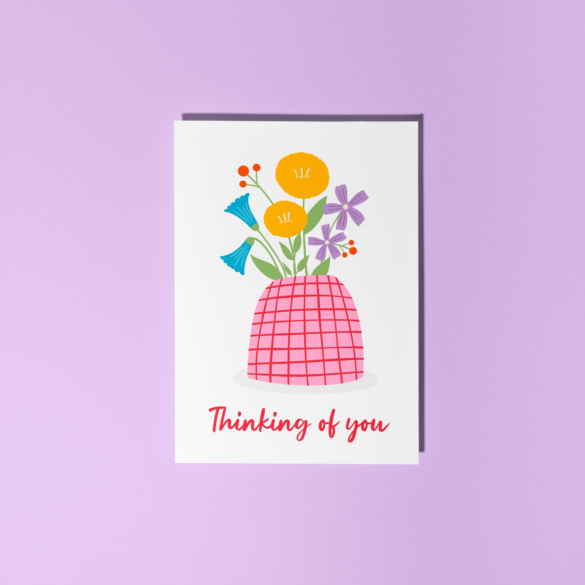 A card with a vase of colourful flowers, on a white background, with red hand written text underneath saying 'thinking of you'.