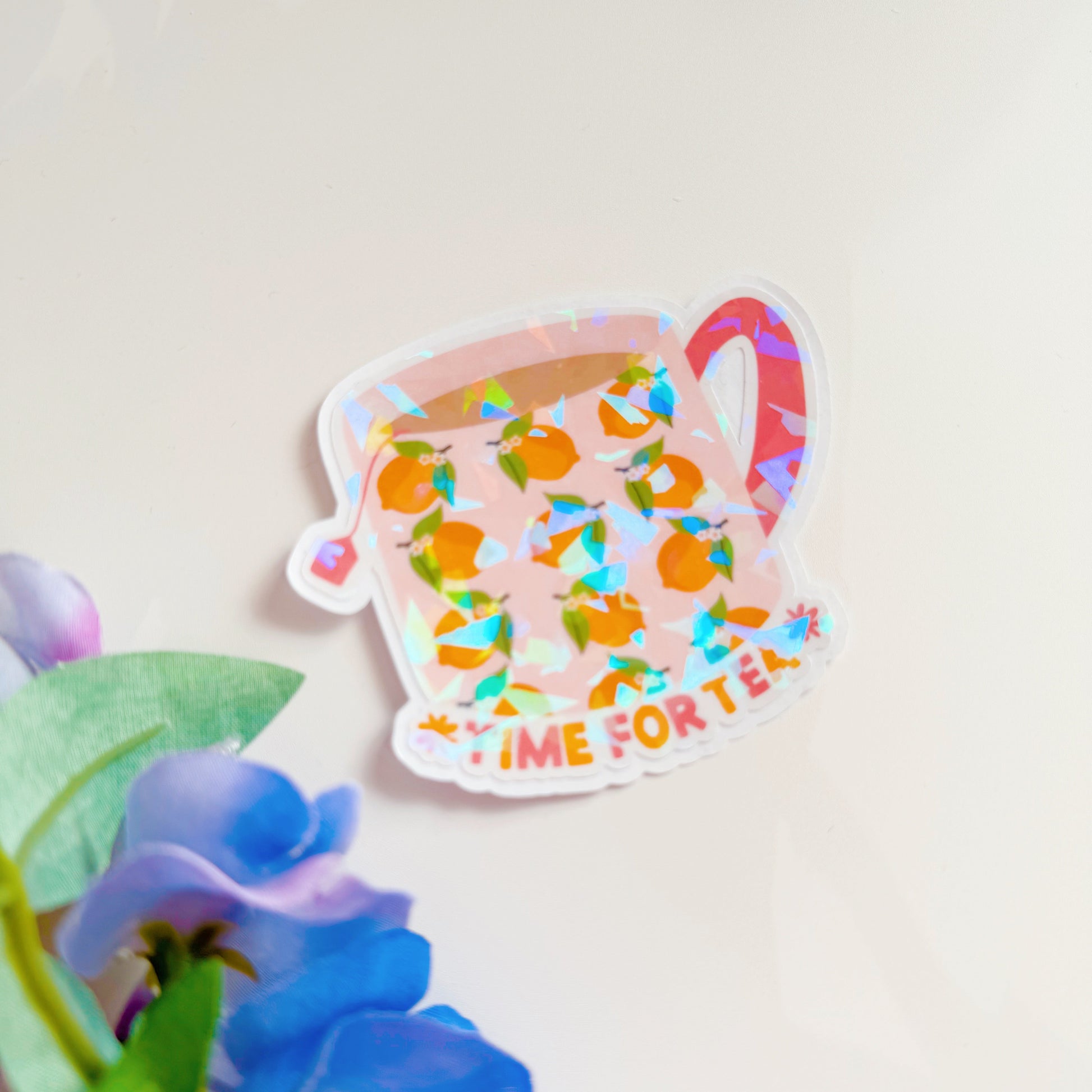 A holographic sticker, with a mug with lemons on it, and text underneath saying 'time for tea'. The sticker has an easy peel lip.