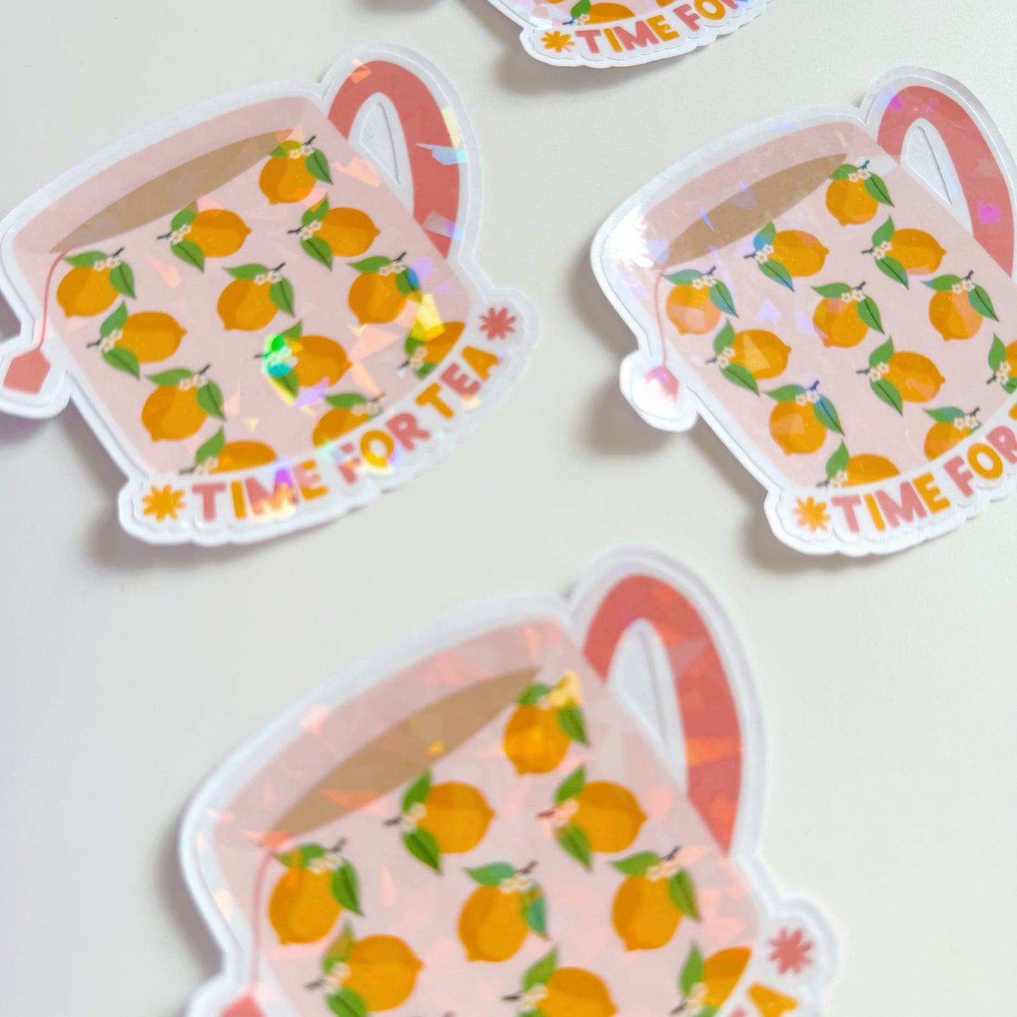 A holographic sticker, with a mug with lemons on it, and text underneath saying 'time for tea'. The sticker has an easy peel lip.