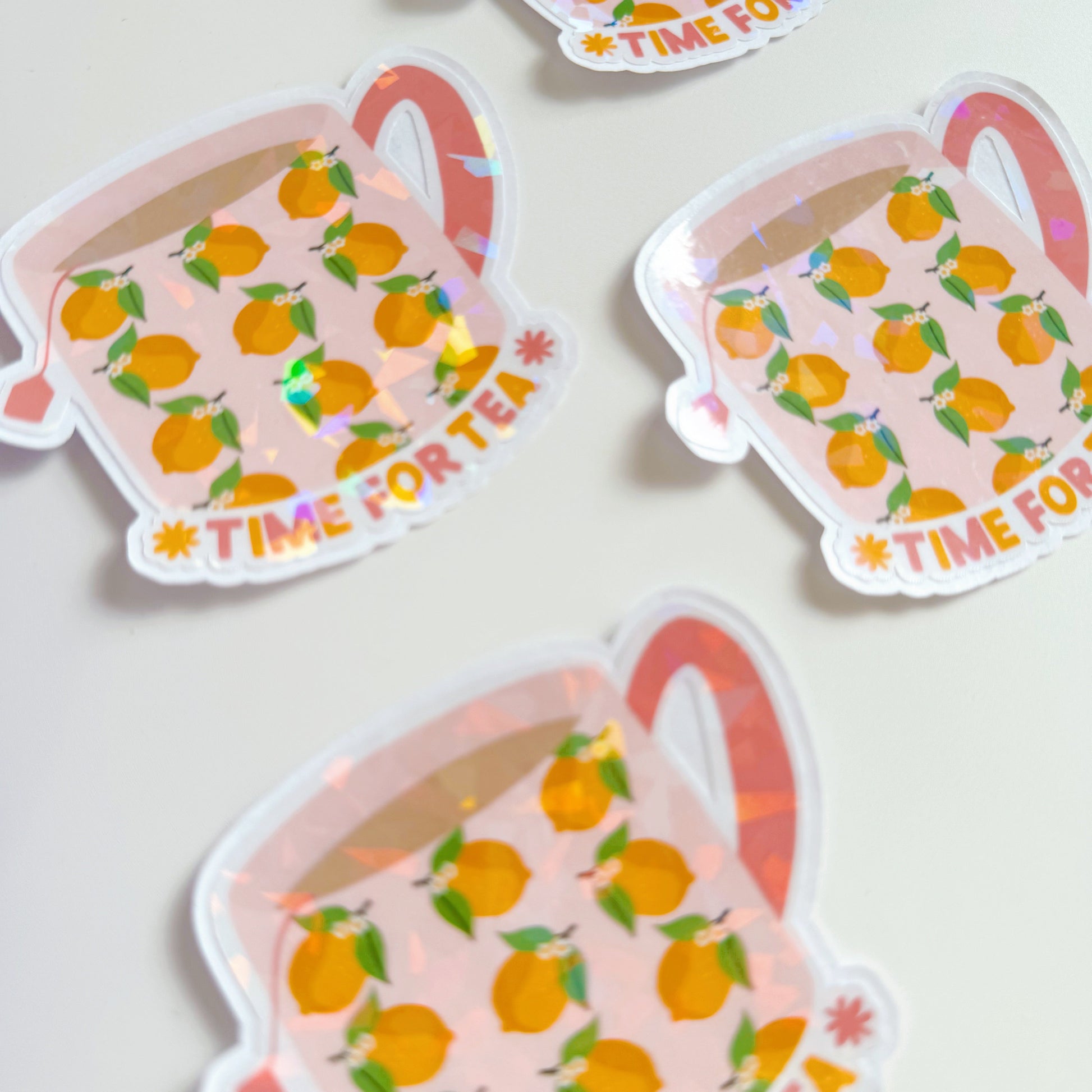 A holographic sticker, with a mug with lemons on it, and text underneath saying 'time for tea'. The sticker has an easy peel lip.