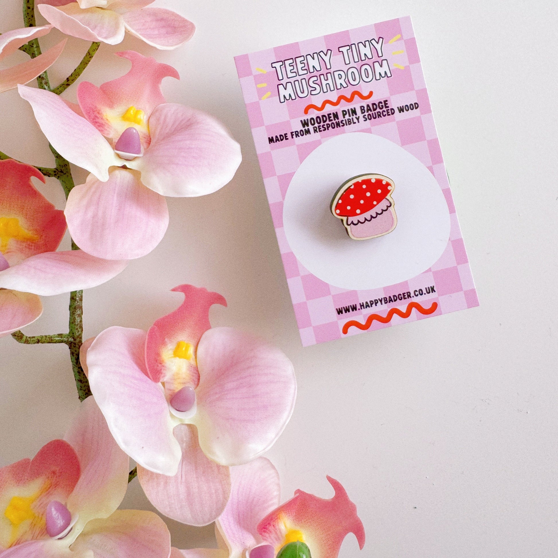 A tiny mushroom shaped wooden pin badge, in pink and white.