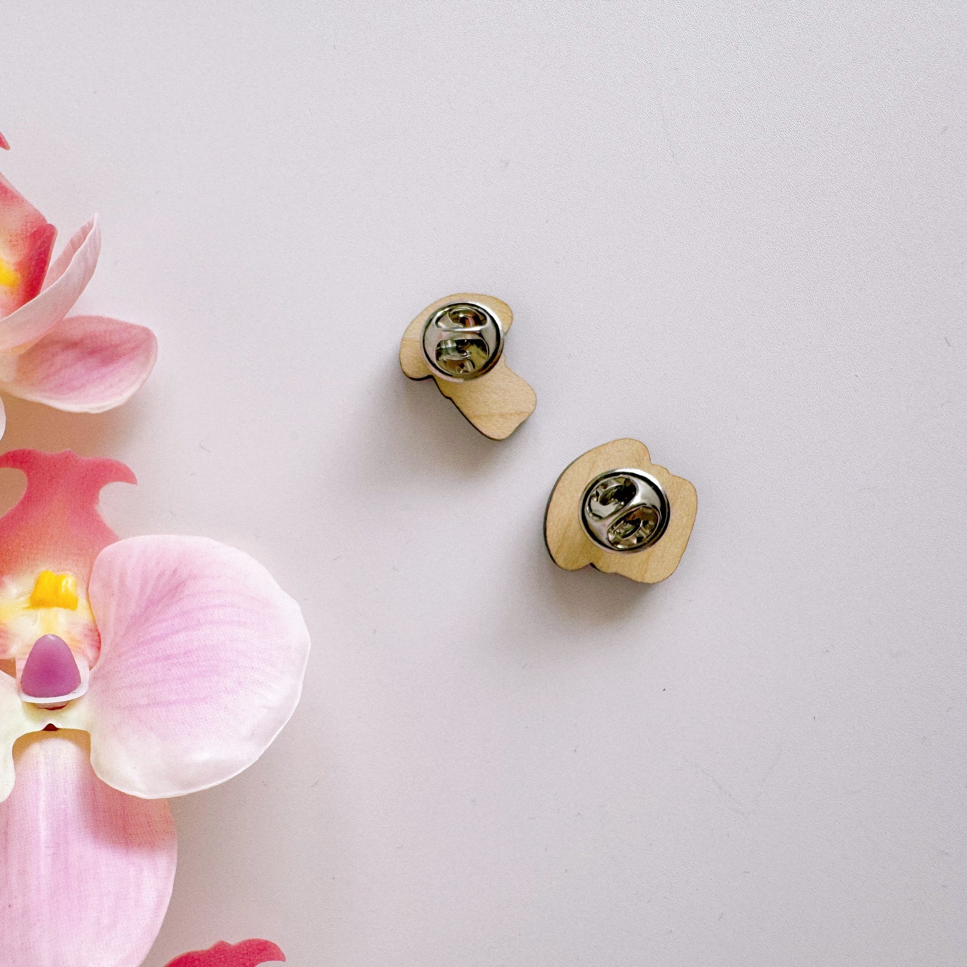 The back side of two tiny mushroom pin badges.