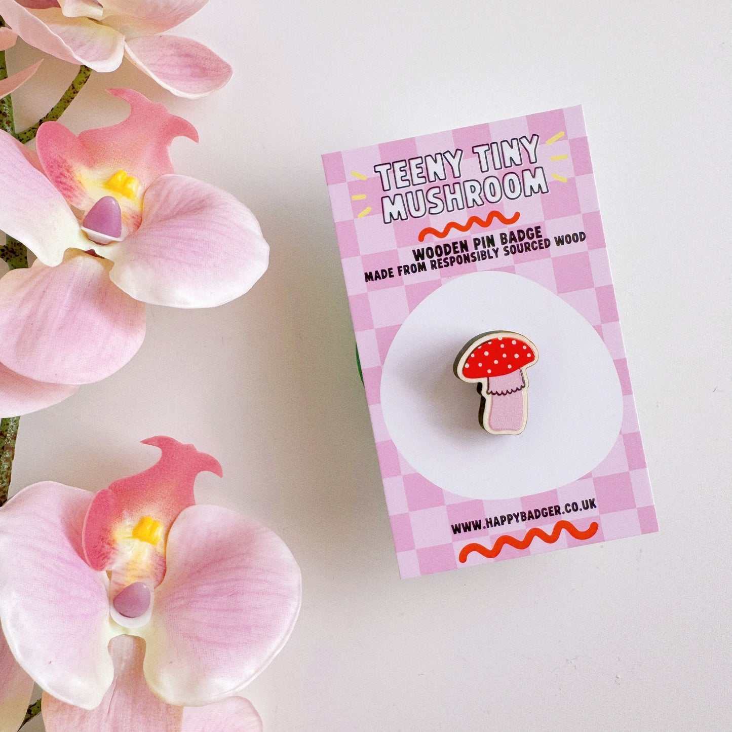 A tiny mushroom shaped wooden pin badge, in pink and white.