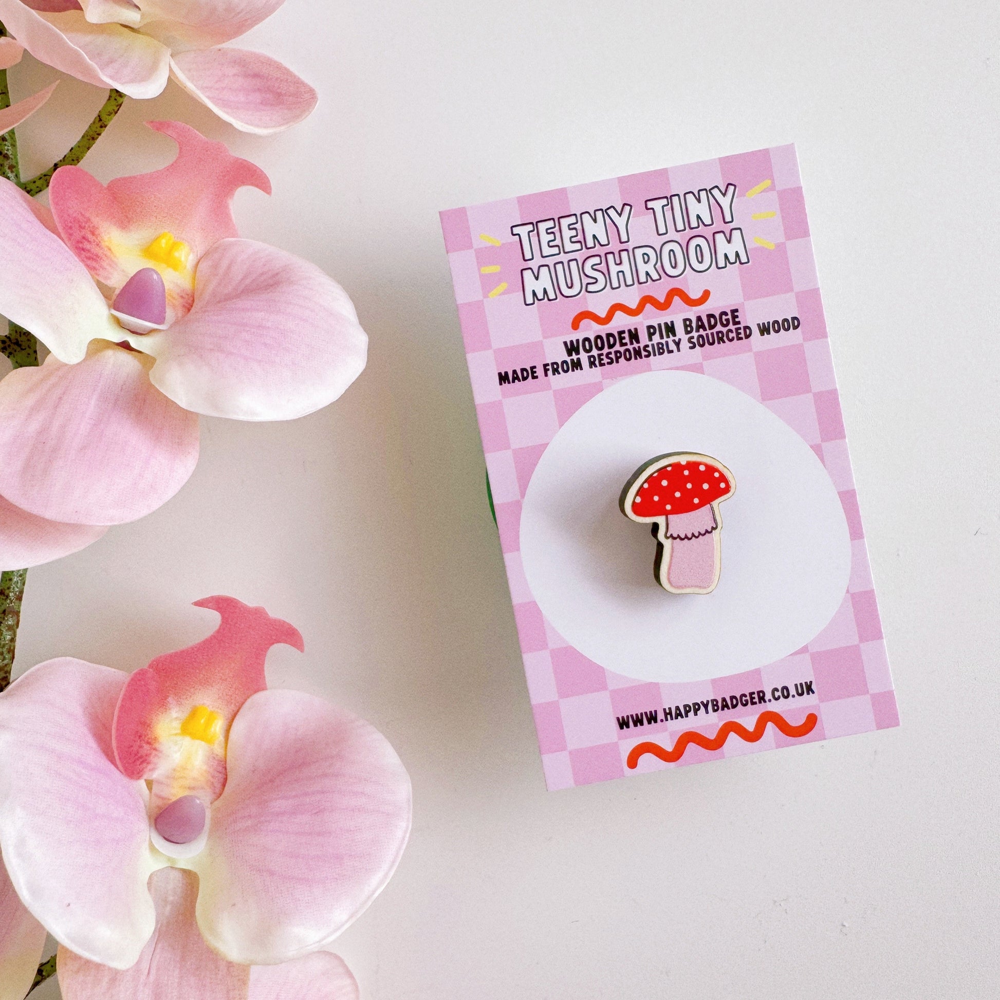 A tiny mushroom shaped wooden pin badge, in pink and white.