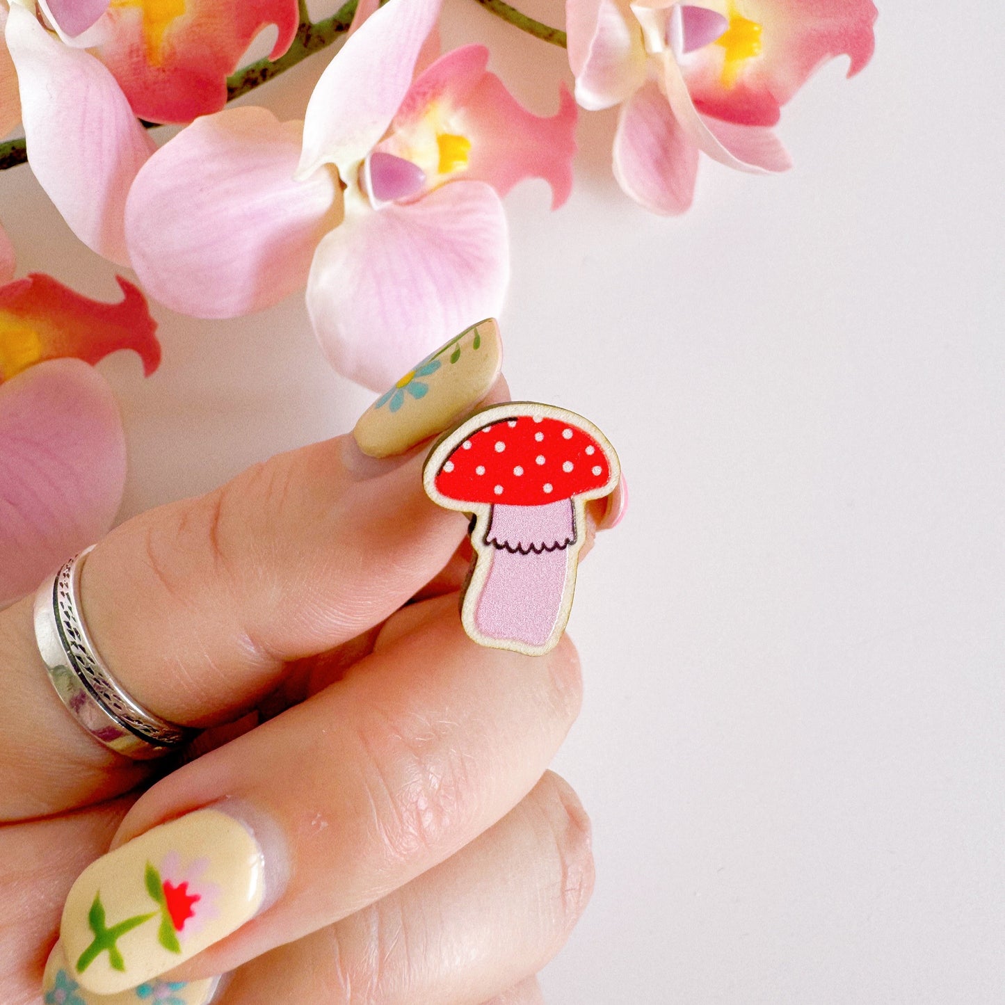 A tiny mushroom shaped wooden pin badge, in pink and white.