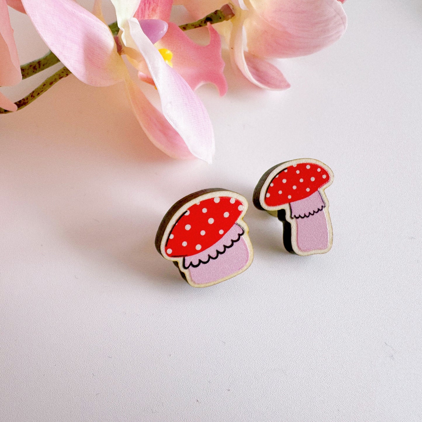 Two tiny mushroom shaped wooden pin badge, in pink and white.