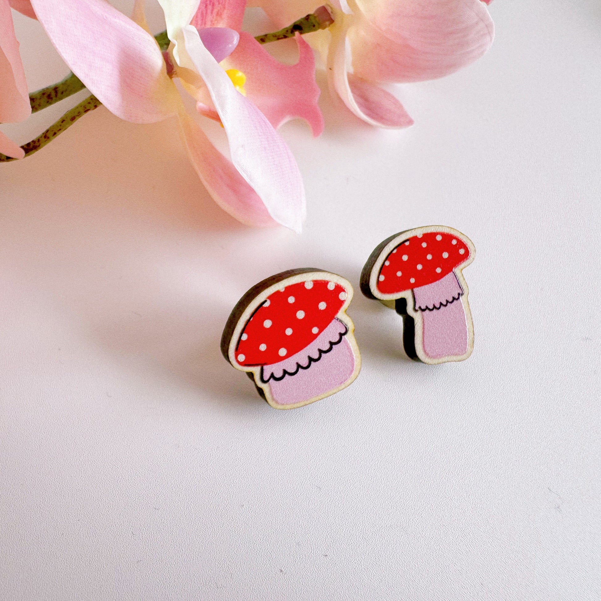 Two tiny mushroom shaped wooden pin badge, in pink and white.