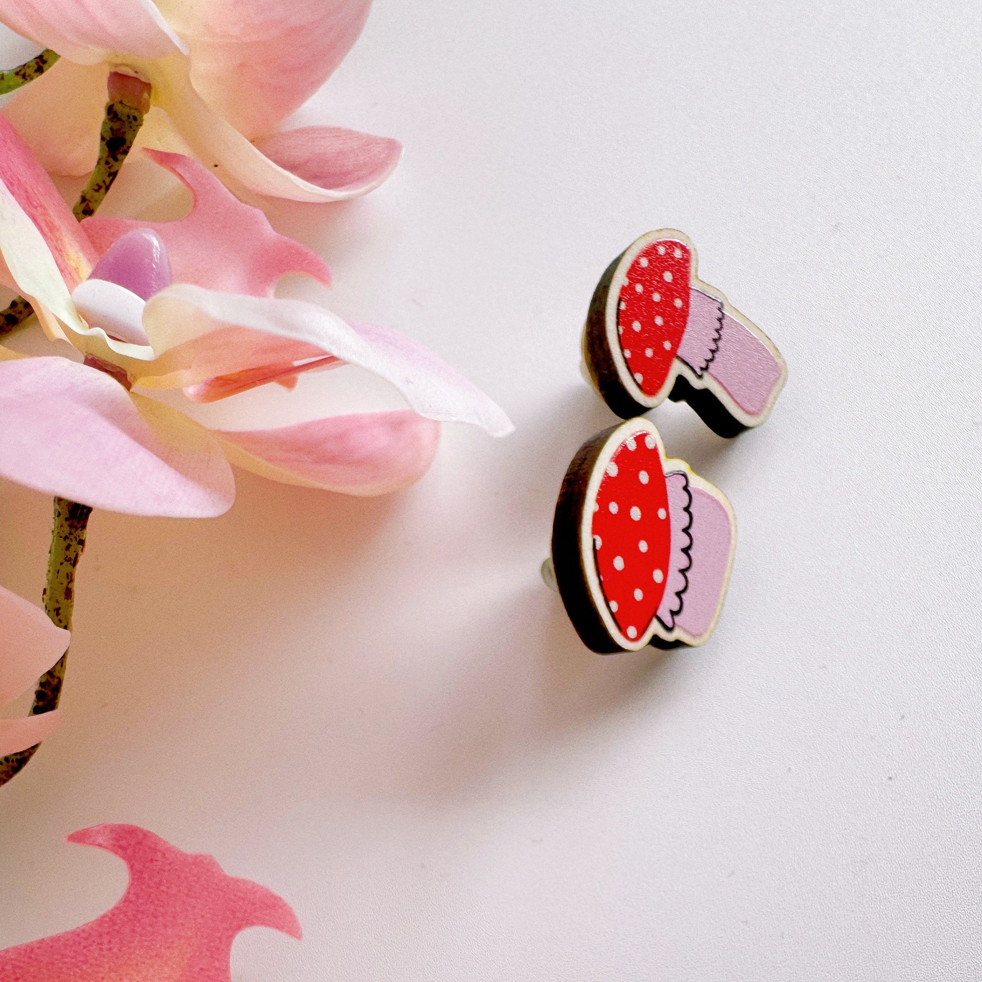 Two tiny mushroom shaped wooden pin badges, in pink and white.