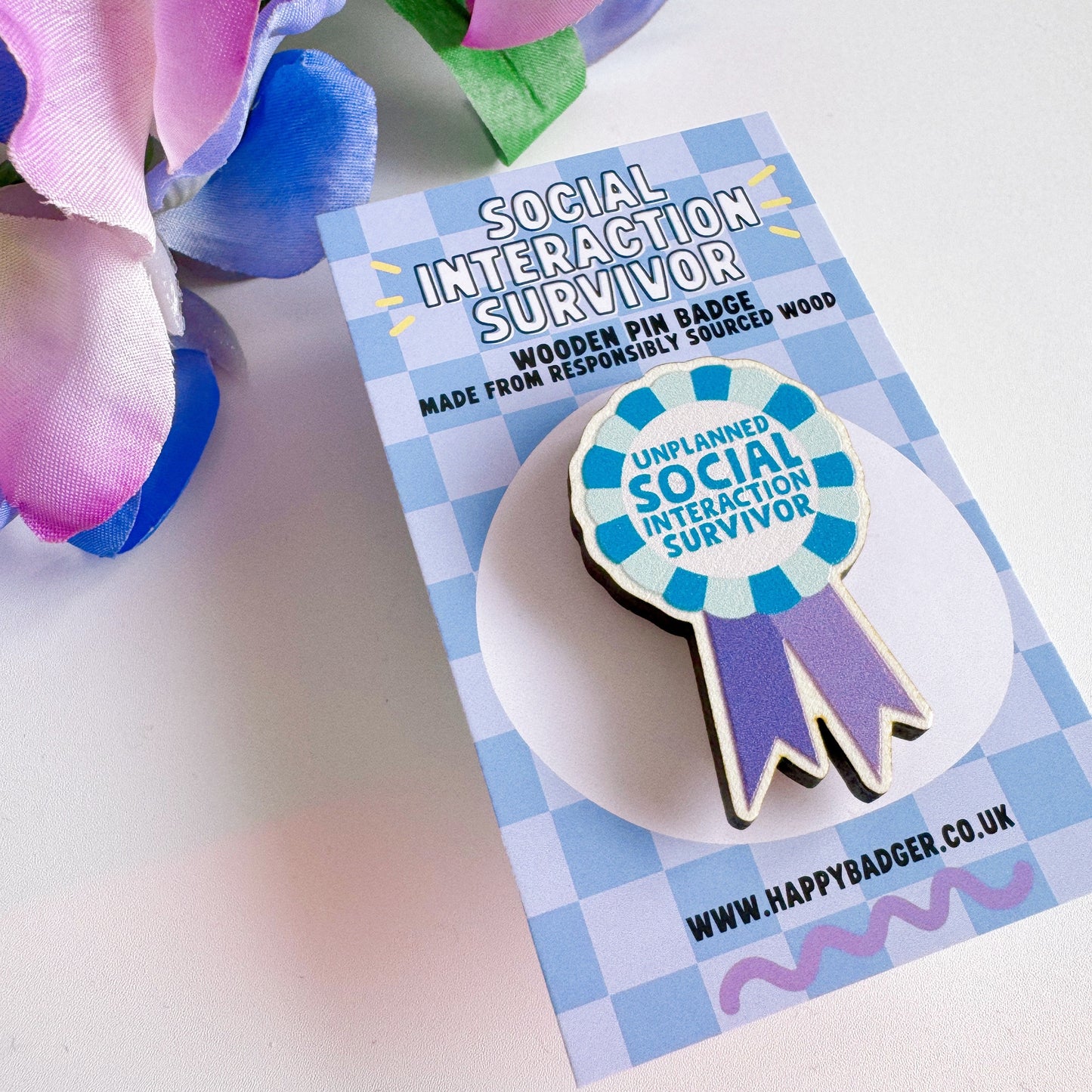 A wooden pin badge, shaped like an award rosette, that says 'unplanned social interaction survivor'.