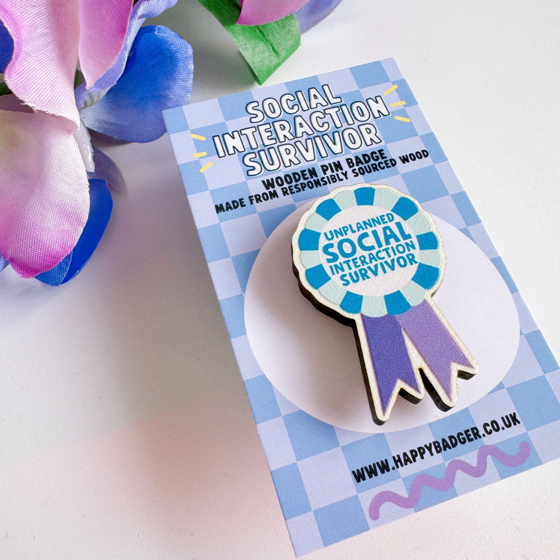 A wooden pin badge, shaped like an award rosette, that says 'unplanned social interaction survivor'.