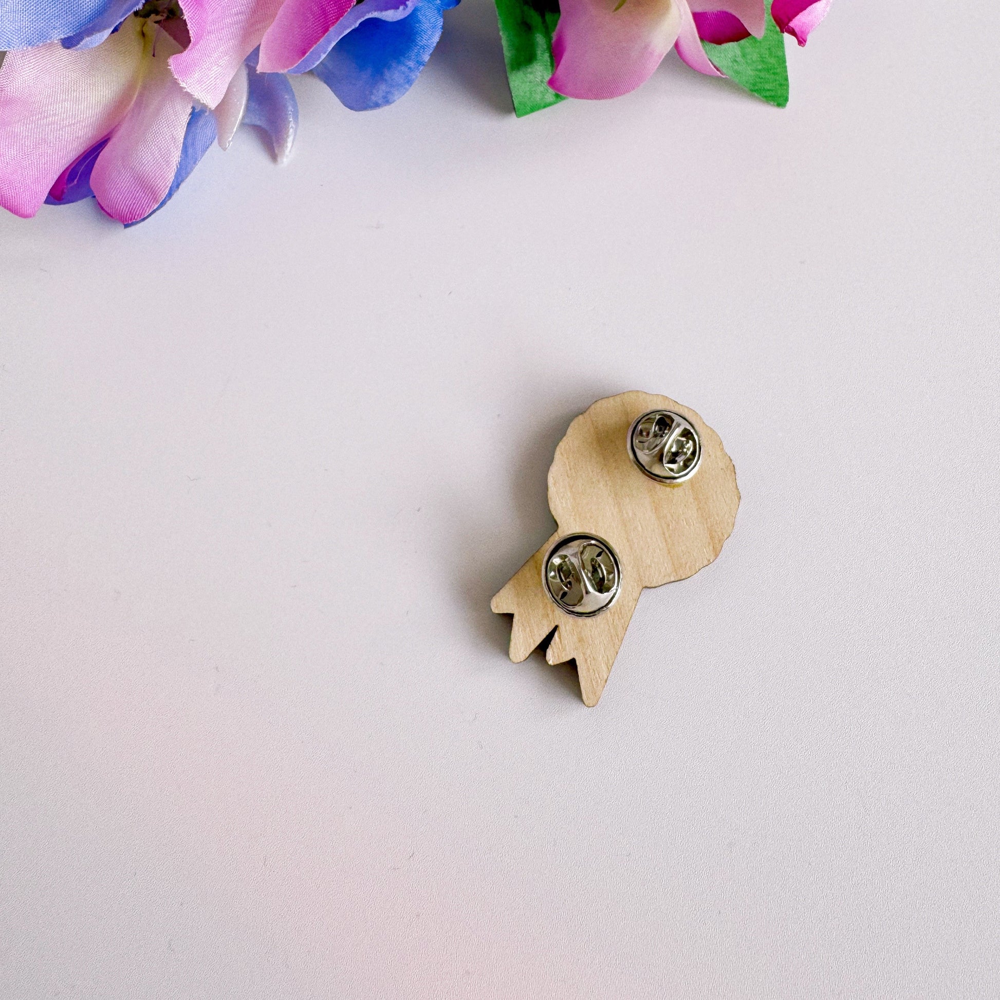 A wooden pin badge, shaped like an award rosette, that says 'unplanned social interaction survivor'.