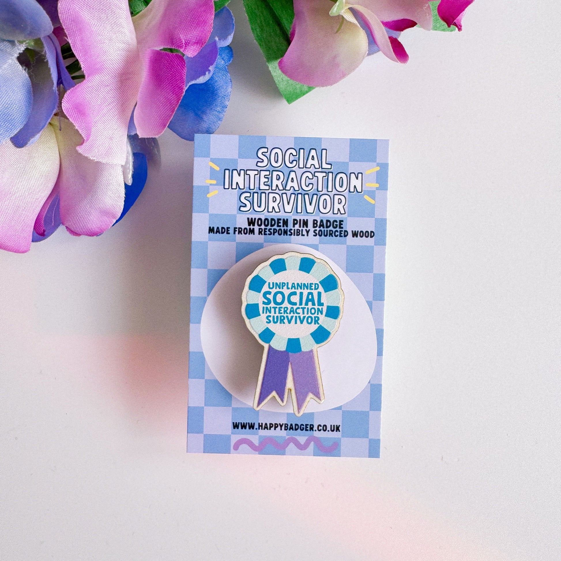 A wooden pin badge, shaped like an award rosette, that says 'unplanned social interaction survivor'.