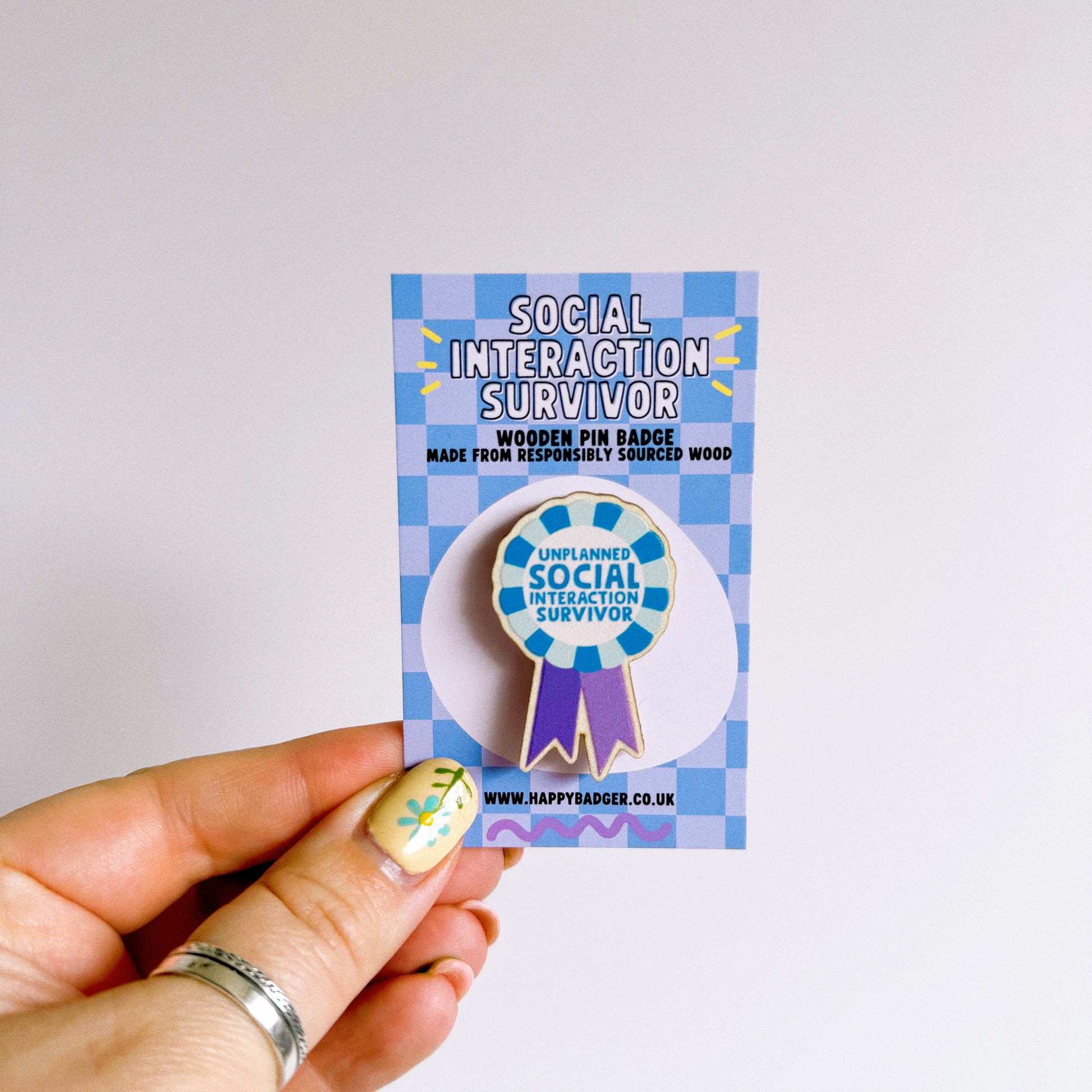 A wooden pin badge, shaped like an award rosette, that says 'unplanned social interaction survivor'.