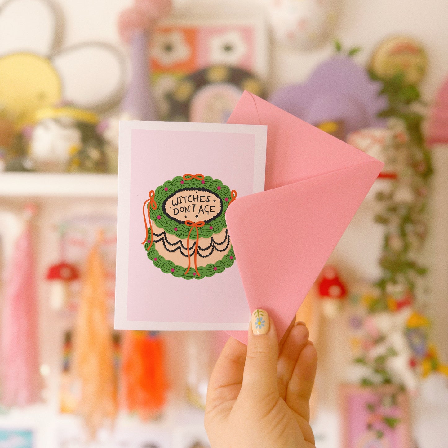 a card with an illustration of a birthday cake, in green and orange, with the words 'witches don't age' on top.