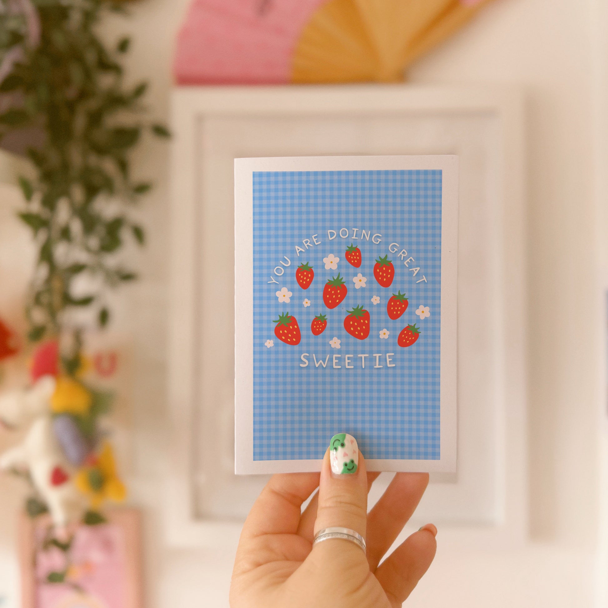 Card with strawberry design and text that reads 'you are doing great sweetie' on a blue gingham background