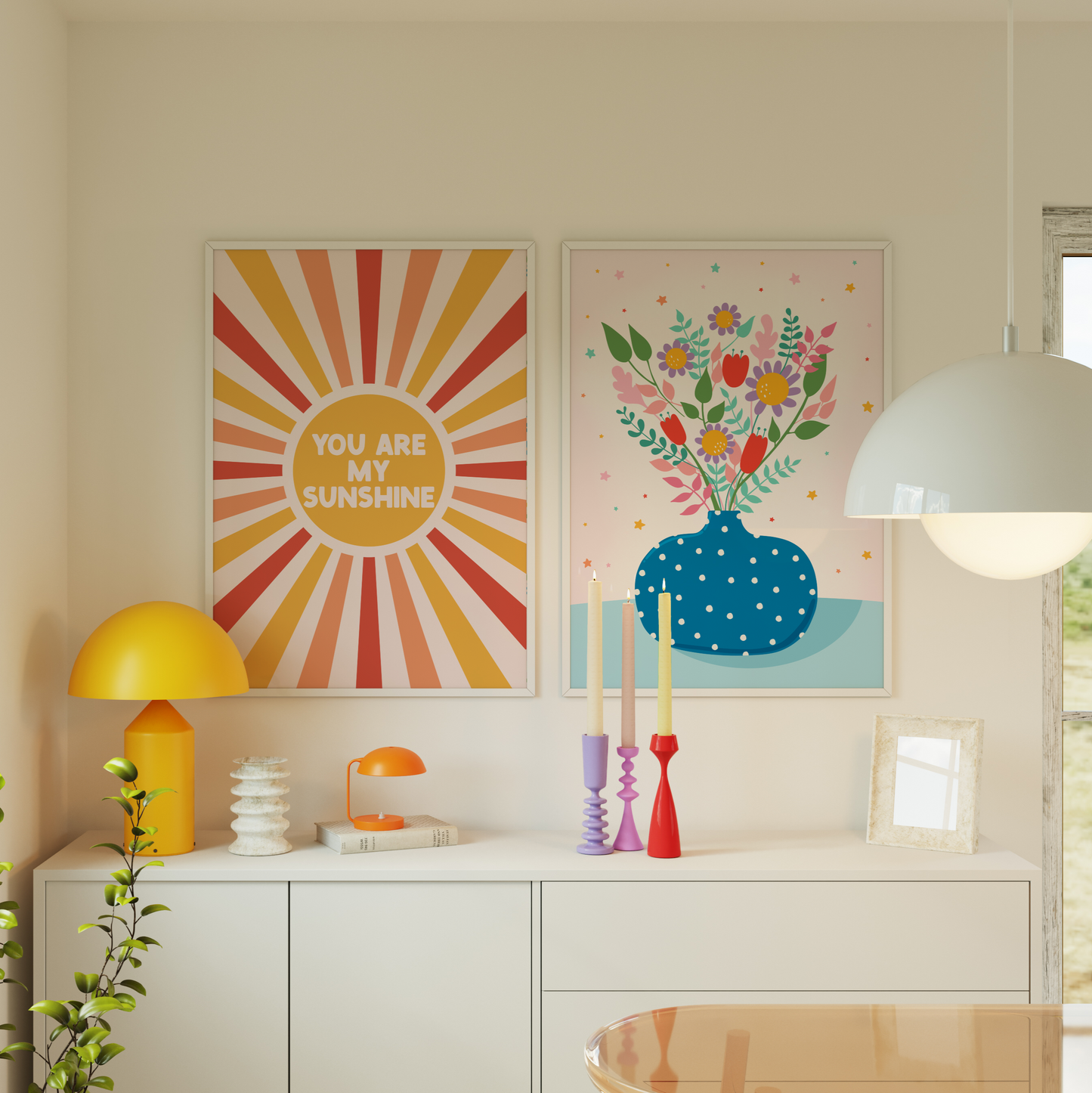 A fun quote print with text saying you are my sunshine, on a star burst background in orange yellow and red. Shown next to a bright blue vase print with colourful vibrant flowers in.