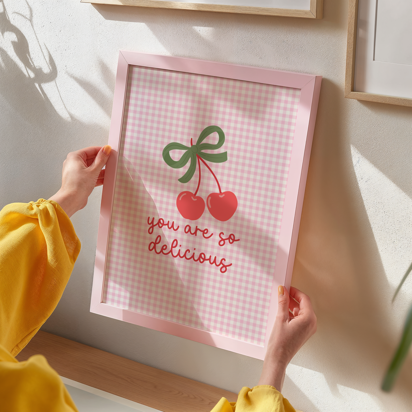 A pink gingham background print, with an illustration of red cherries tied together with a green bow, and the quote saying 'you are so delicious' below.
