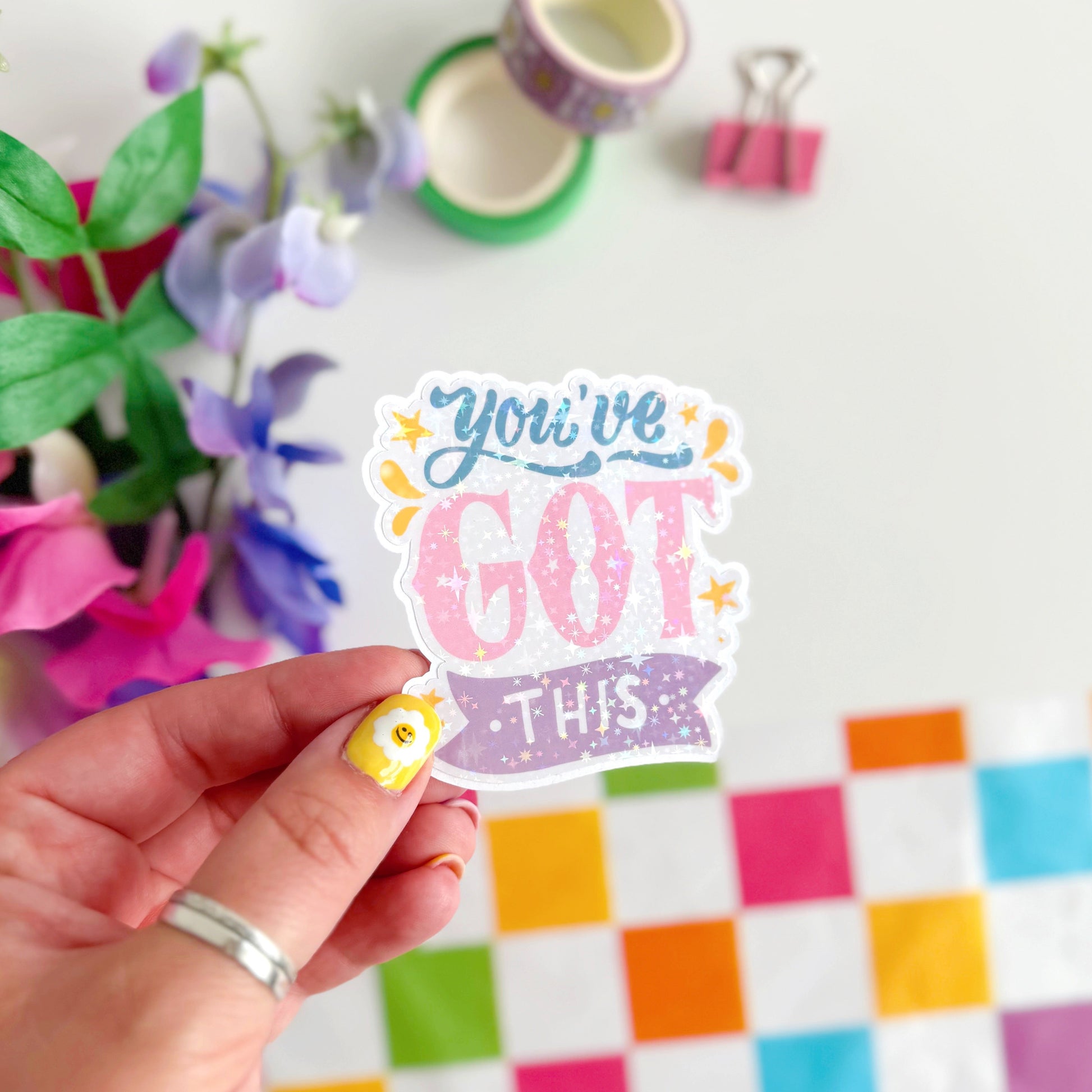 A holographic sticker with script writing saying 'you've got this' in blue, pink and purple, with little yellow illustrated detailing around the text.