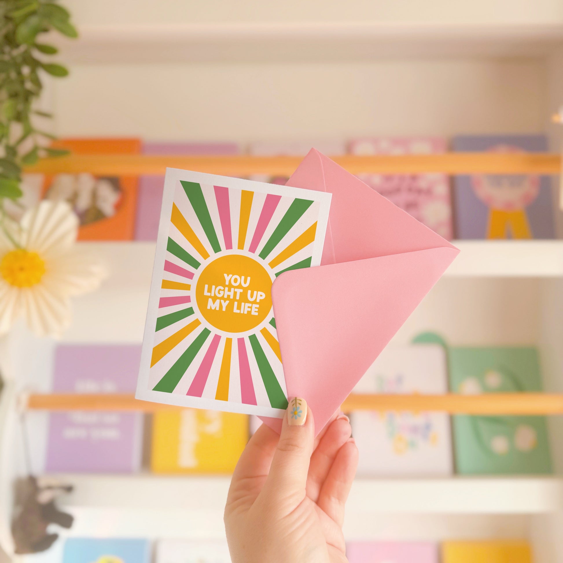 a greetings card with a colourful pink yellow and green sunburst, with the words you light up life in the centre.