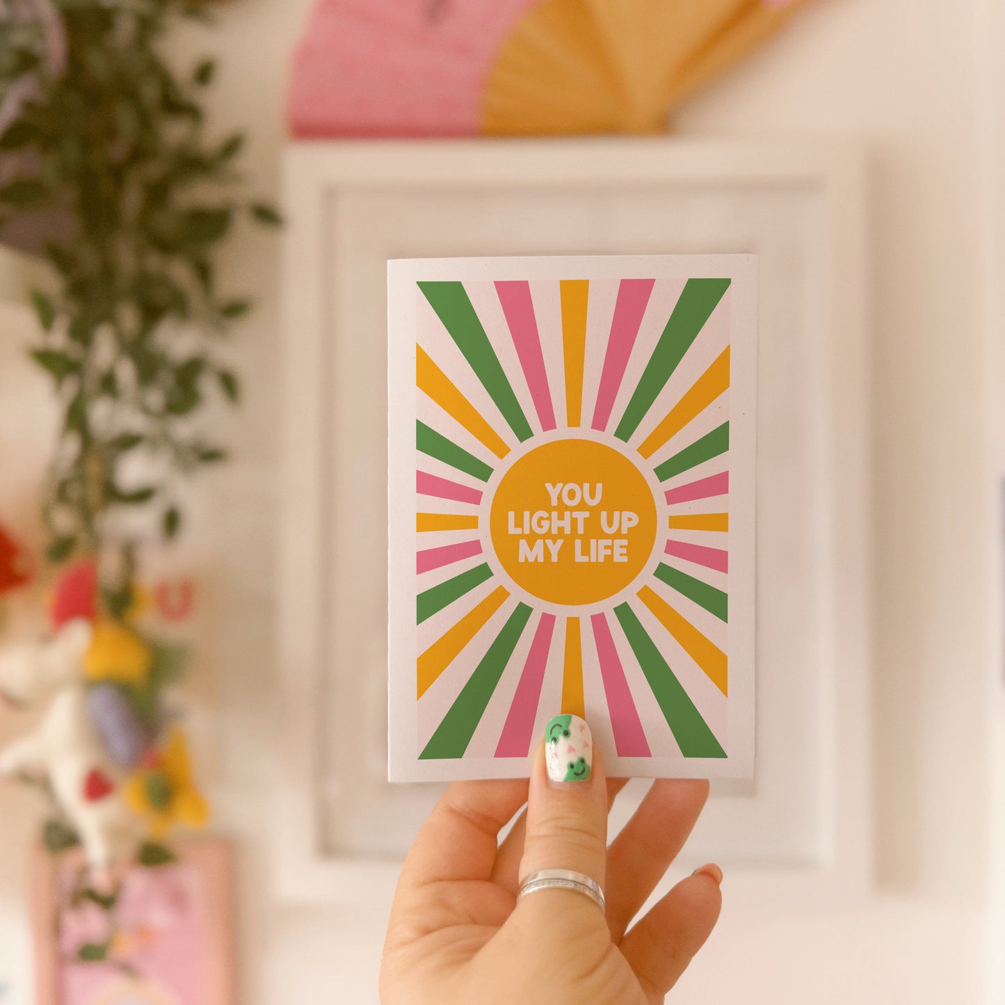 a greetings card with a colourful pink yellow and green sunburst, with the words you light up life in the centre.