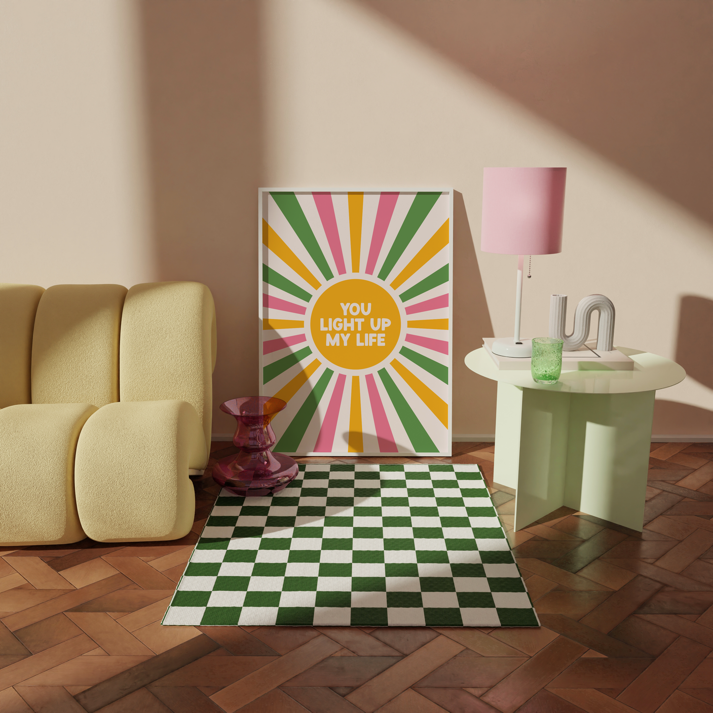A bright vibrant print, showing a sunburst pattern in pink green and yellow, with a yellow circle in the middle saying 'You Light Up My Life'.