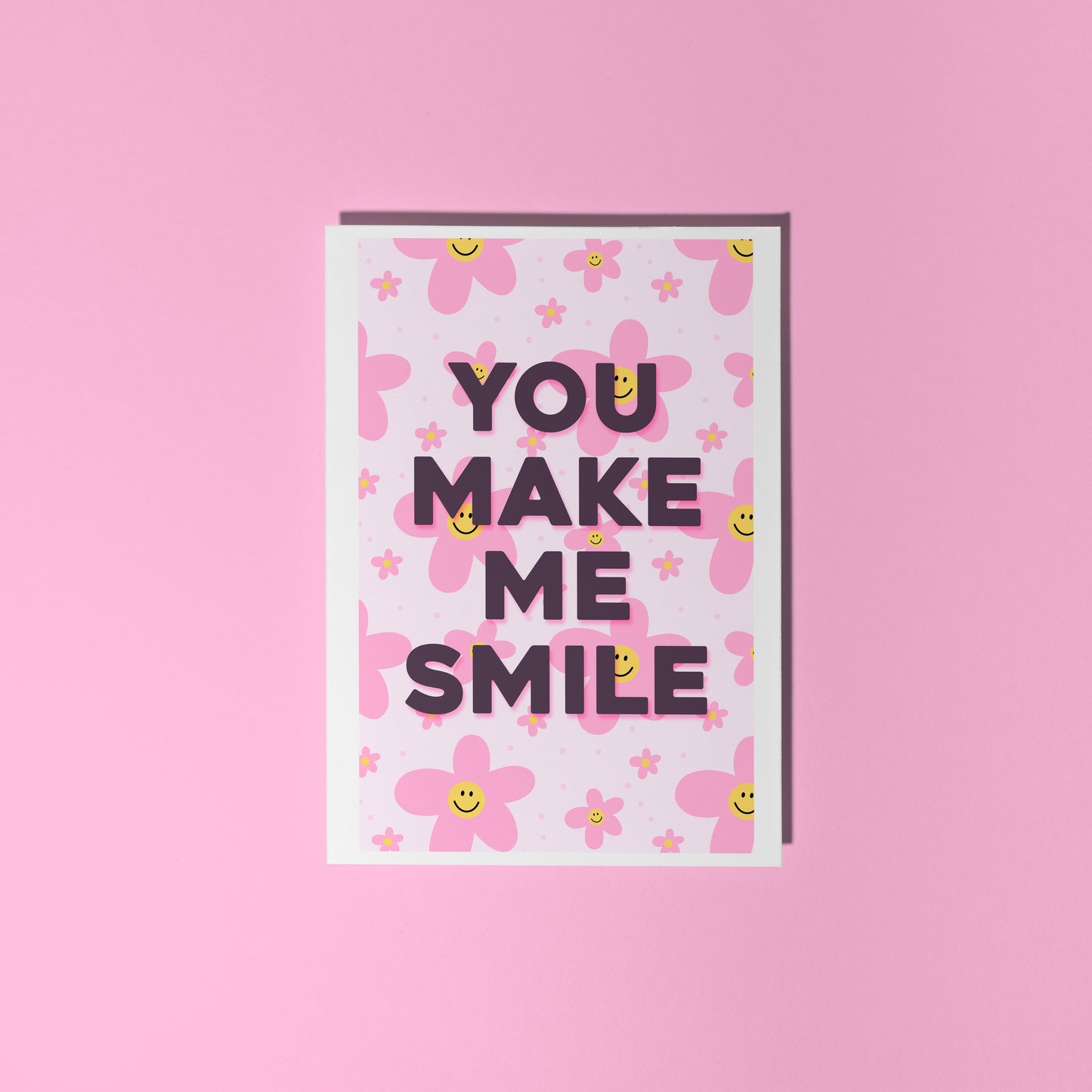 a card with pink smiling daisies on the background, and black text reading 'you make me smile'.