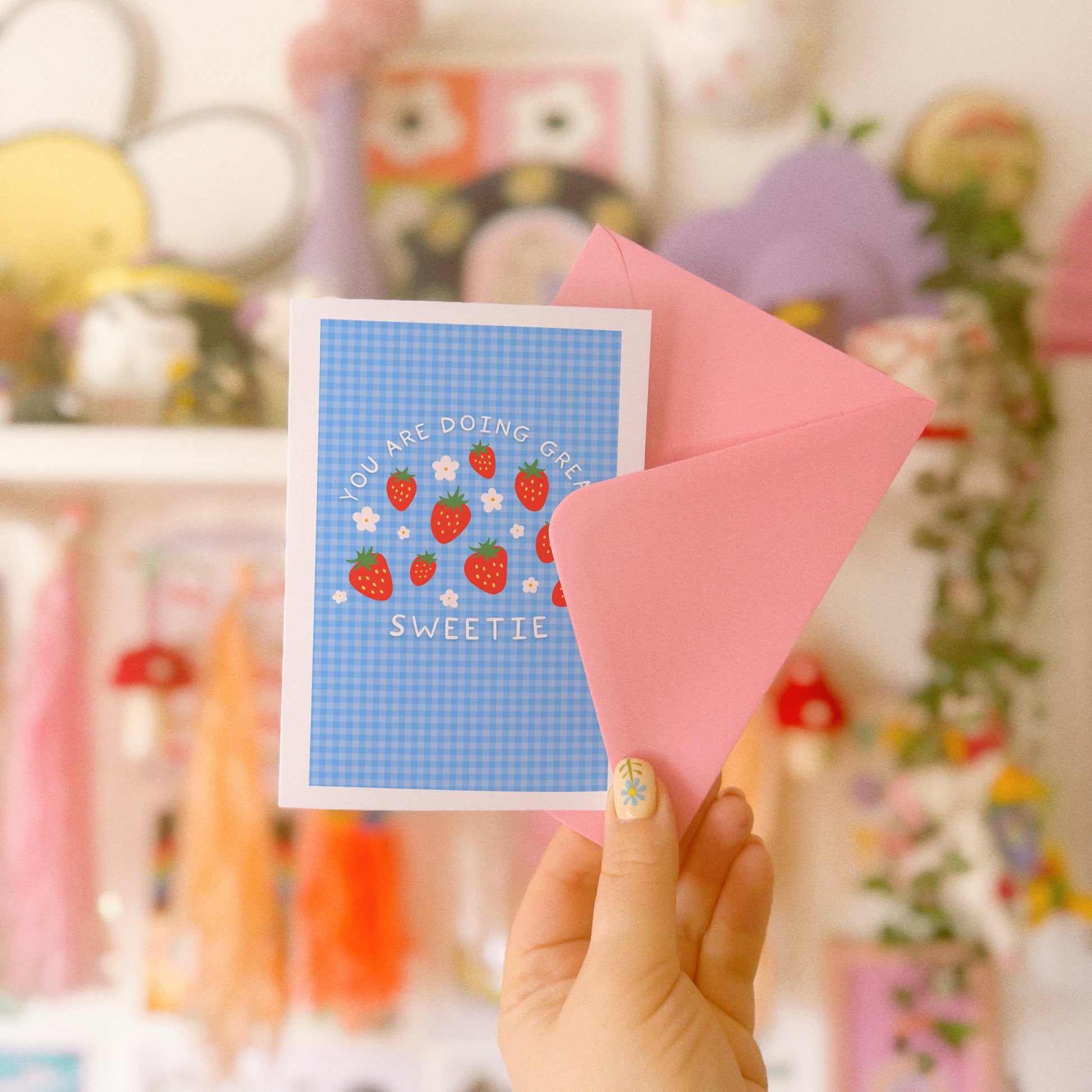 Card with strawberry design and text that reads 'you are doing great sweetie' on a blue gingham background