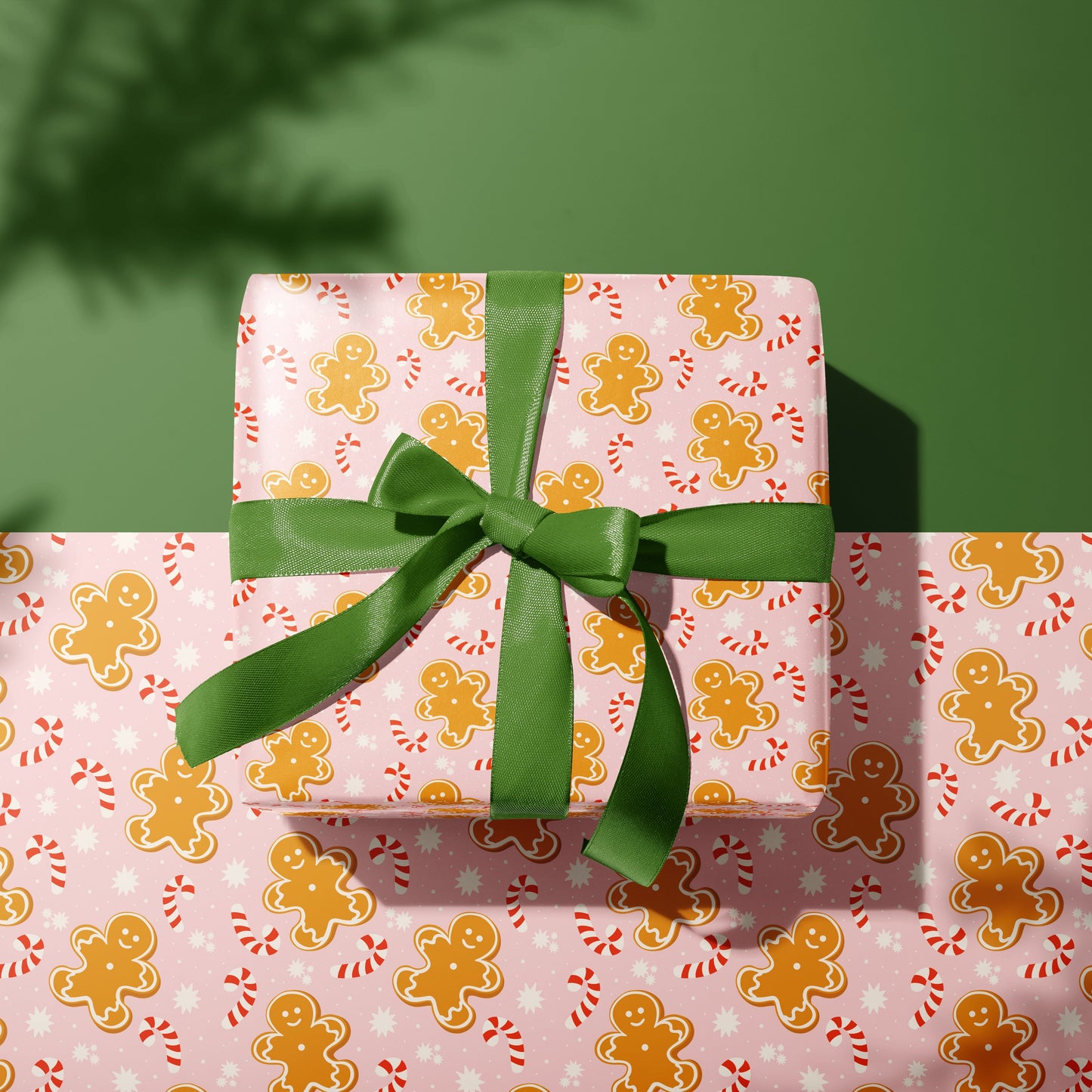 Gift box wrapped in gingerbread man patterned paper with a green ribbon on a matching background.