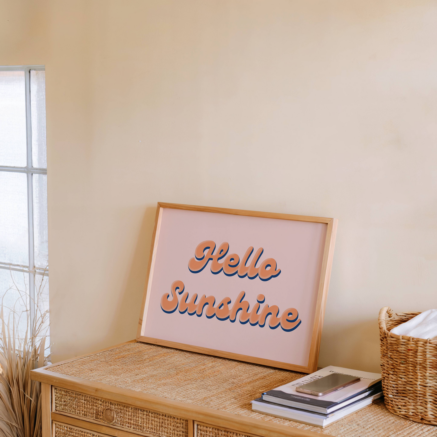 Framed 'Hello Sunshine' art print on a wooden side table with a wicker basket and books.