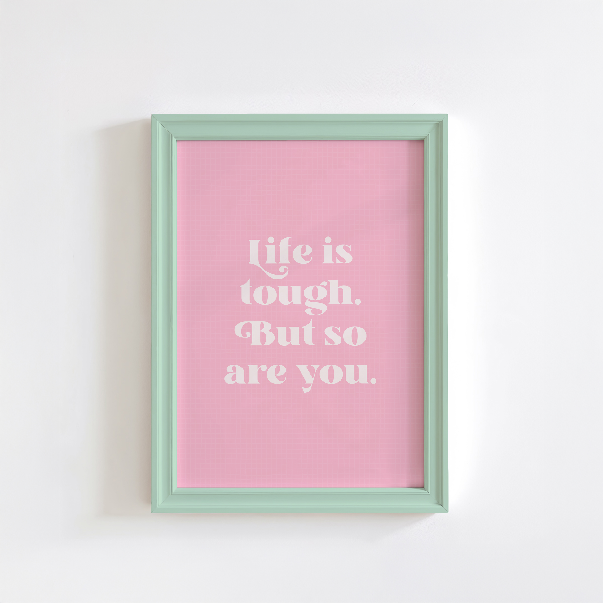 A framed print with a pink background and green frame, containing the text 'Life is tough. But so are you.' in a white font.