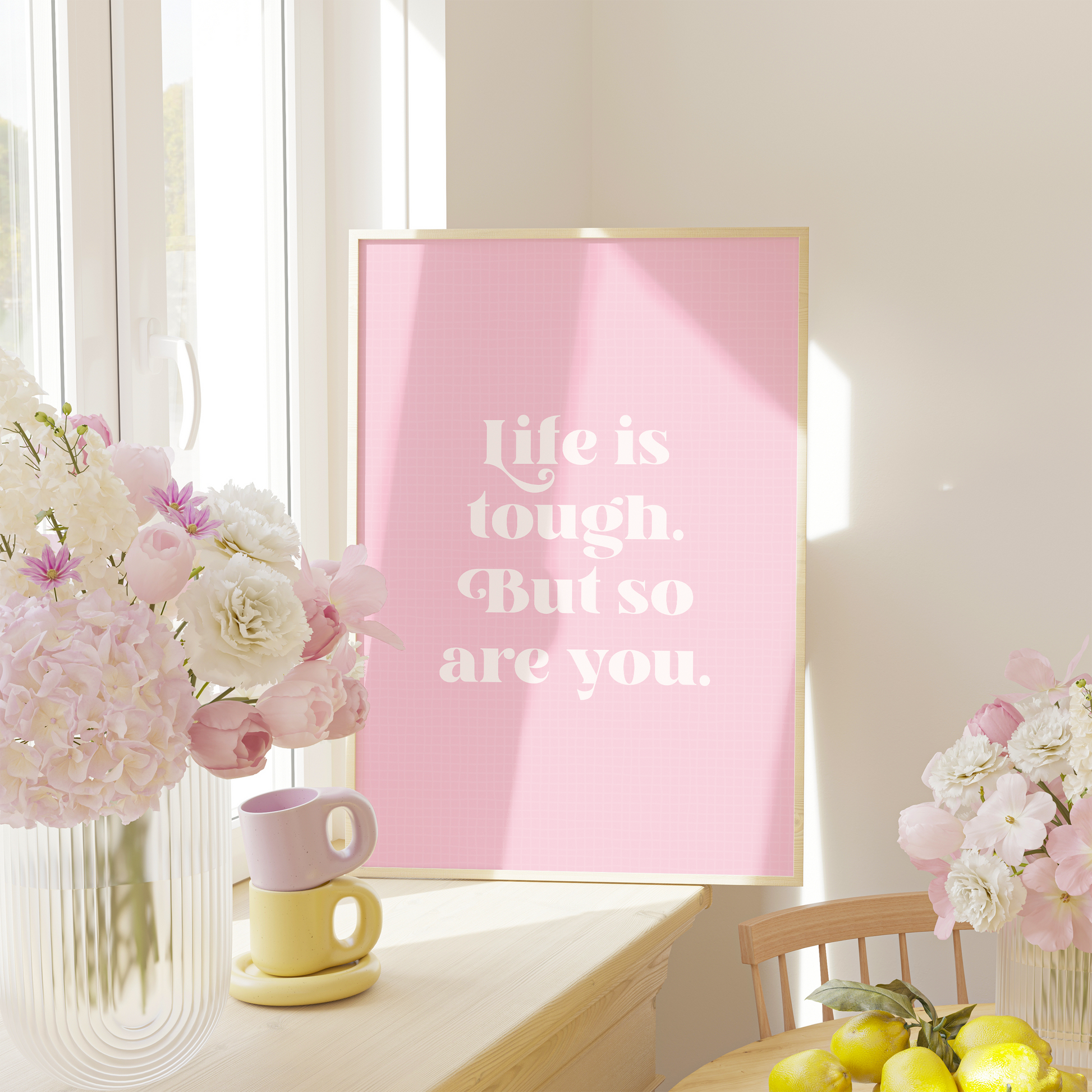 A framed print with a pink background and green frame, containing the text 'Life is tough. But so are you.' in a white font.