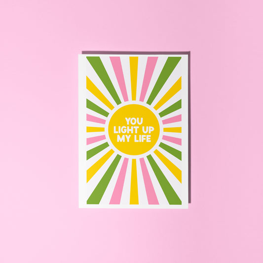 a greetings card with a colourful pink yellow and green sunburst, with the words you light up life in the centre.