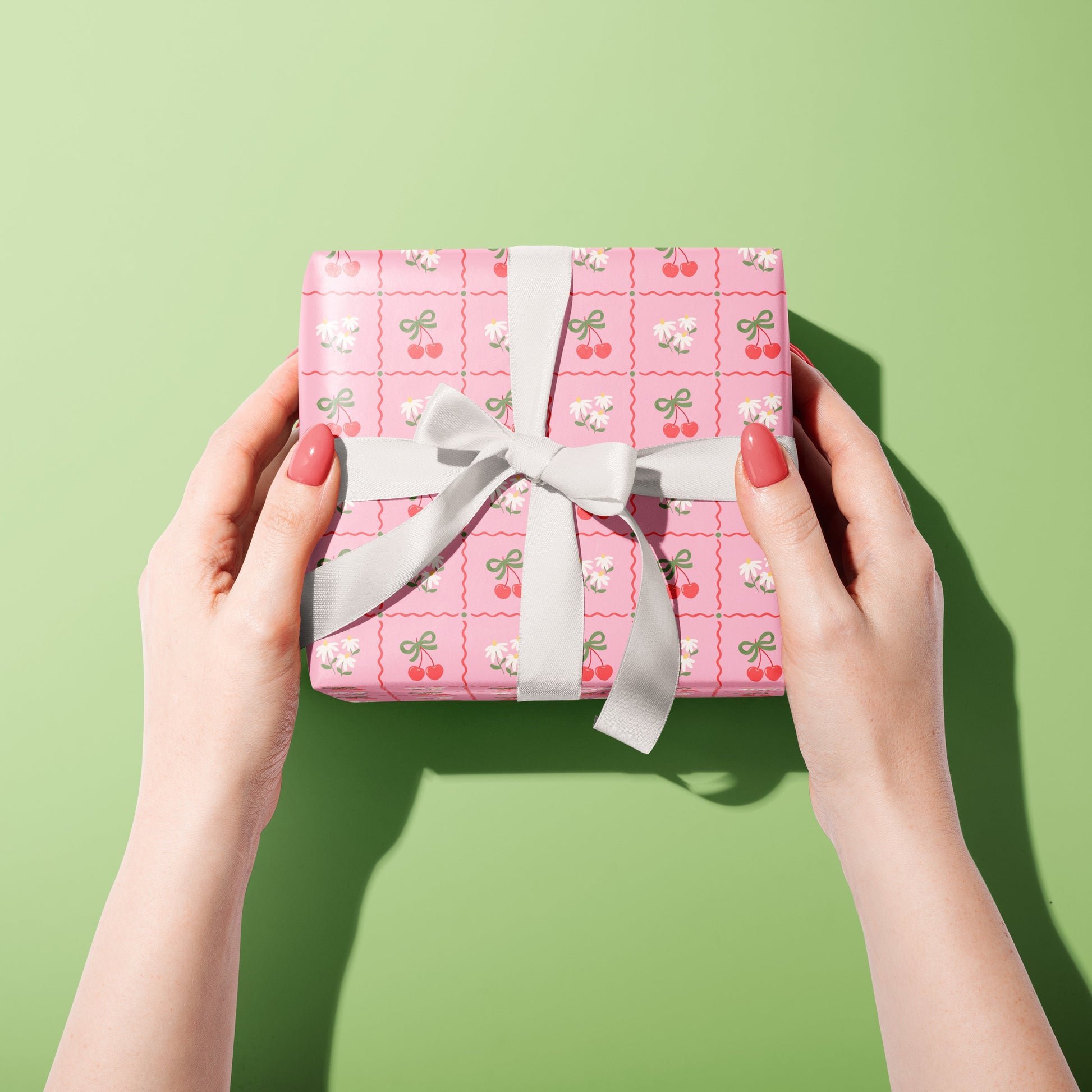 A pink patterned gift wrap, with cherries and daisies on.