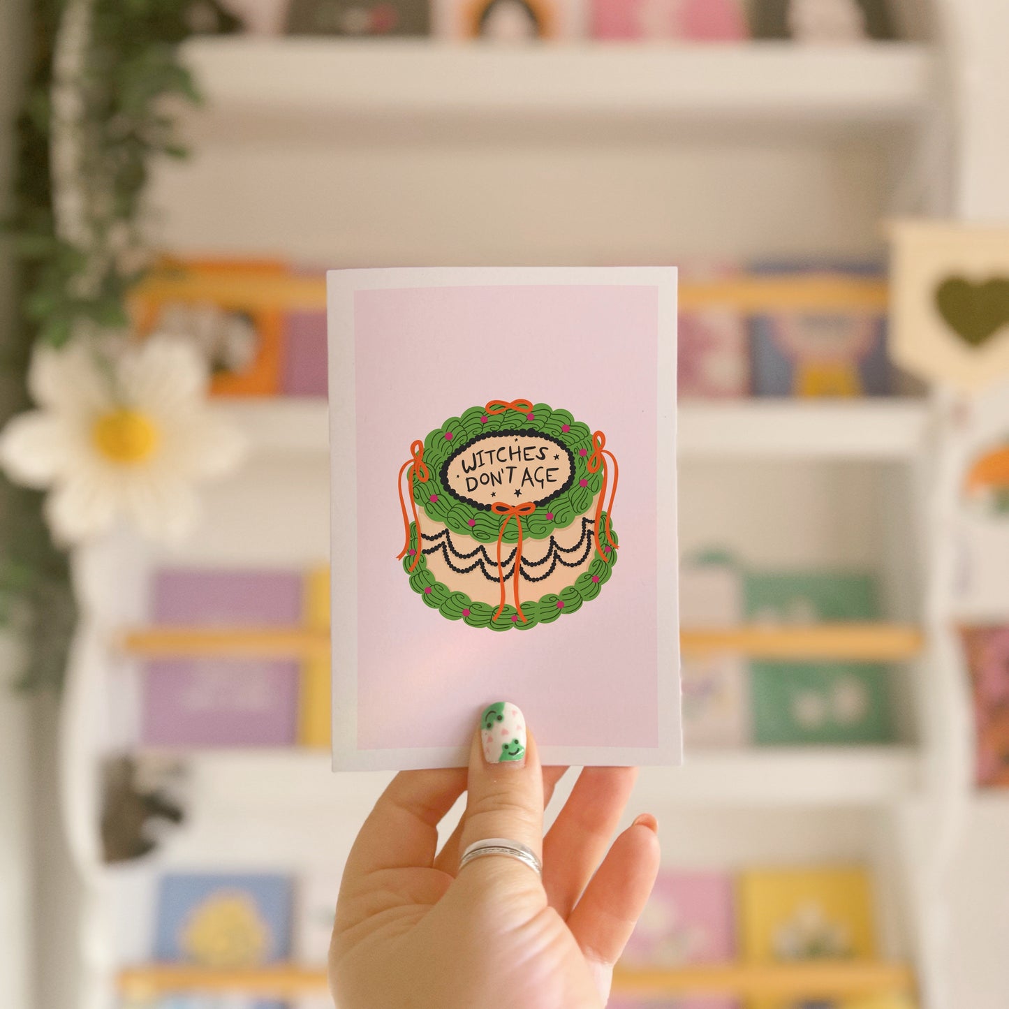 a card with an illustration of a birthday cake, in green and orange, with the words 'witches don't age' on top.
