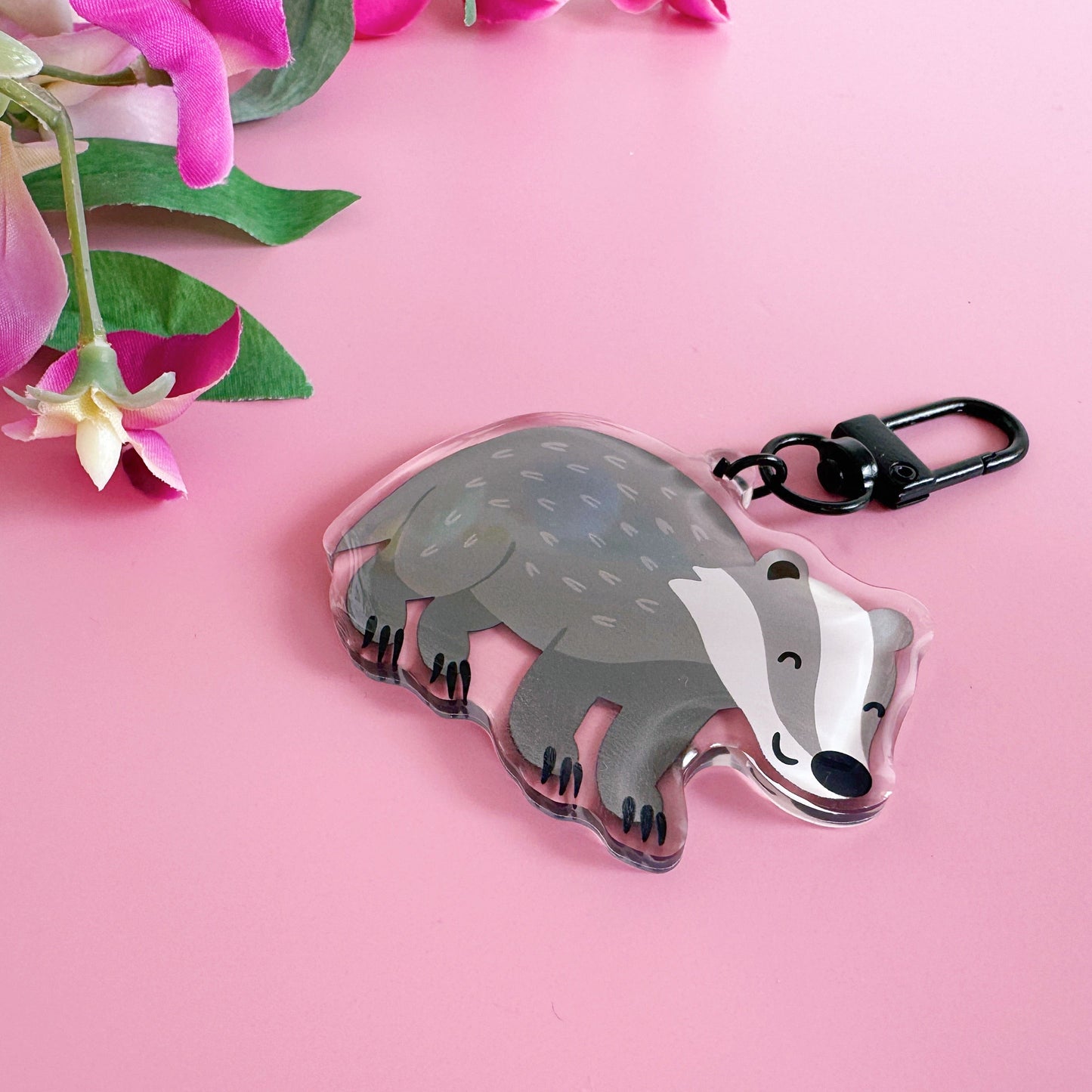 Badger-shaped keychain on a pink background with flowers