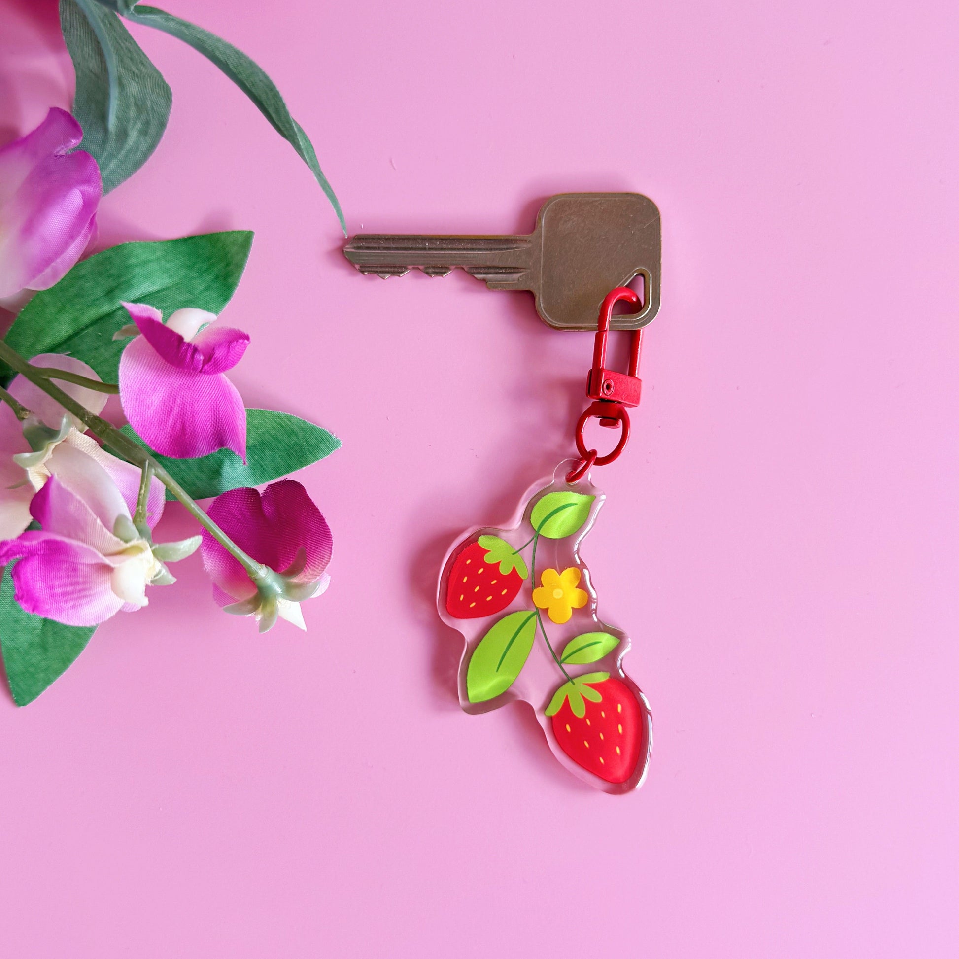 Keychain with strawberry design attached to a key on a pink background with flowers.