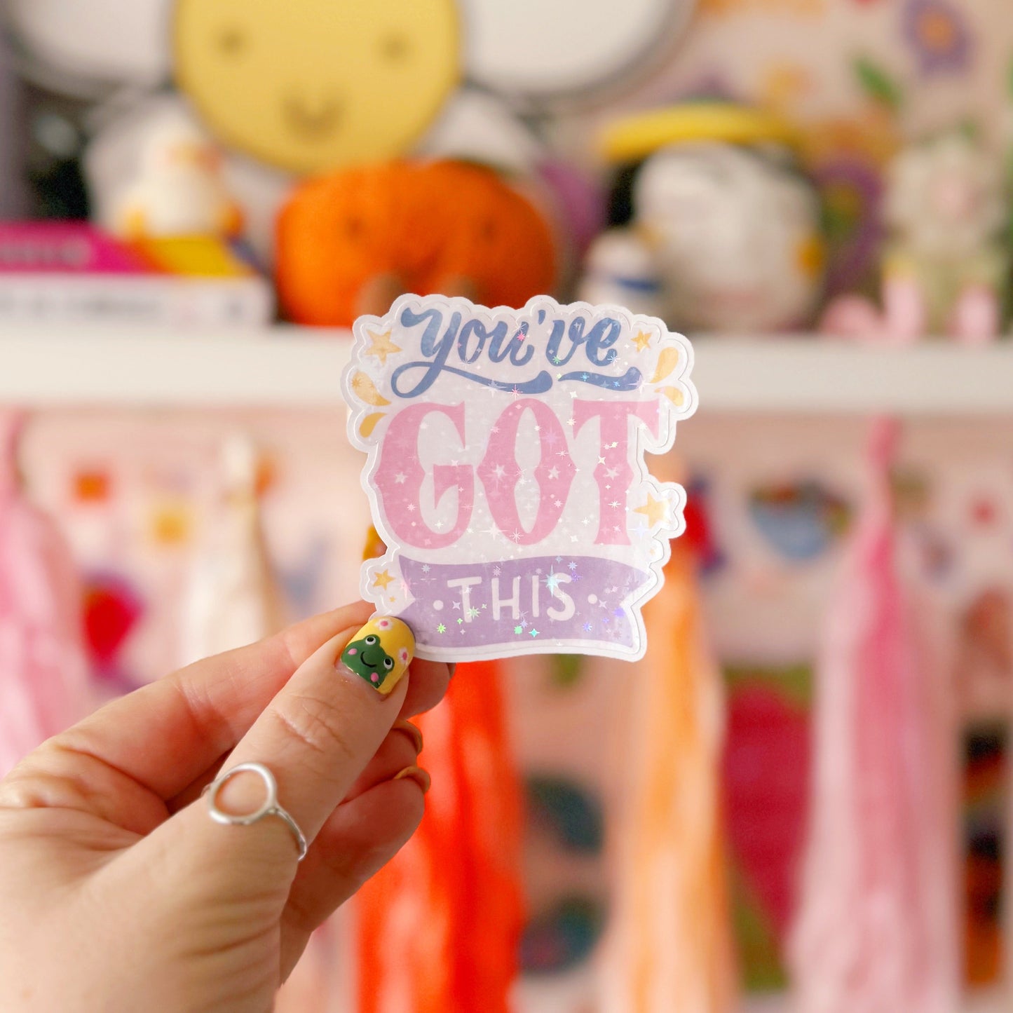 A holographic sticker with script writing saying 'you've got this' in blue, pink and purple, with little yellow illustrated detailing around the text.