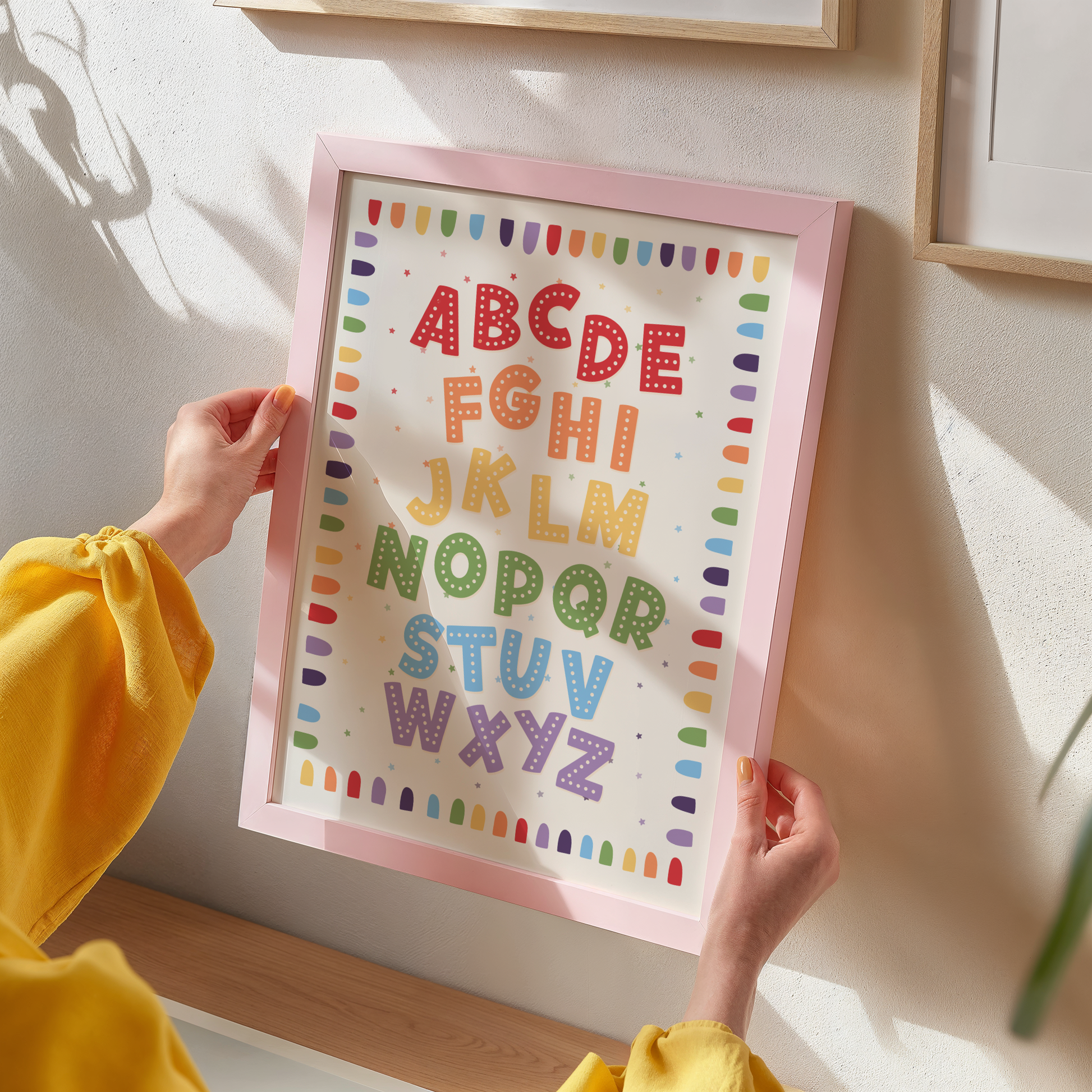 A framed alphabet art print featuring colourful decorative letters A through Z on a cream background, with a decorative border.