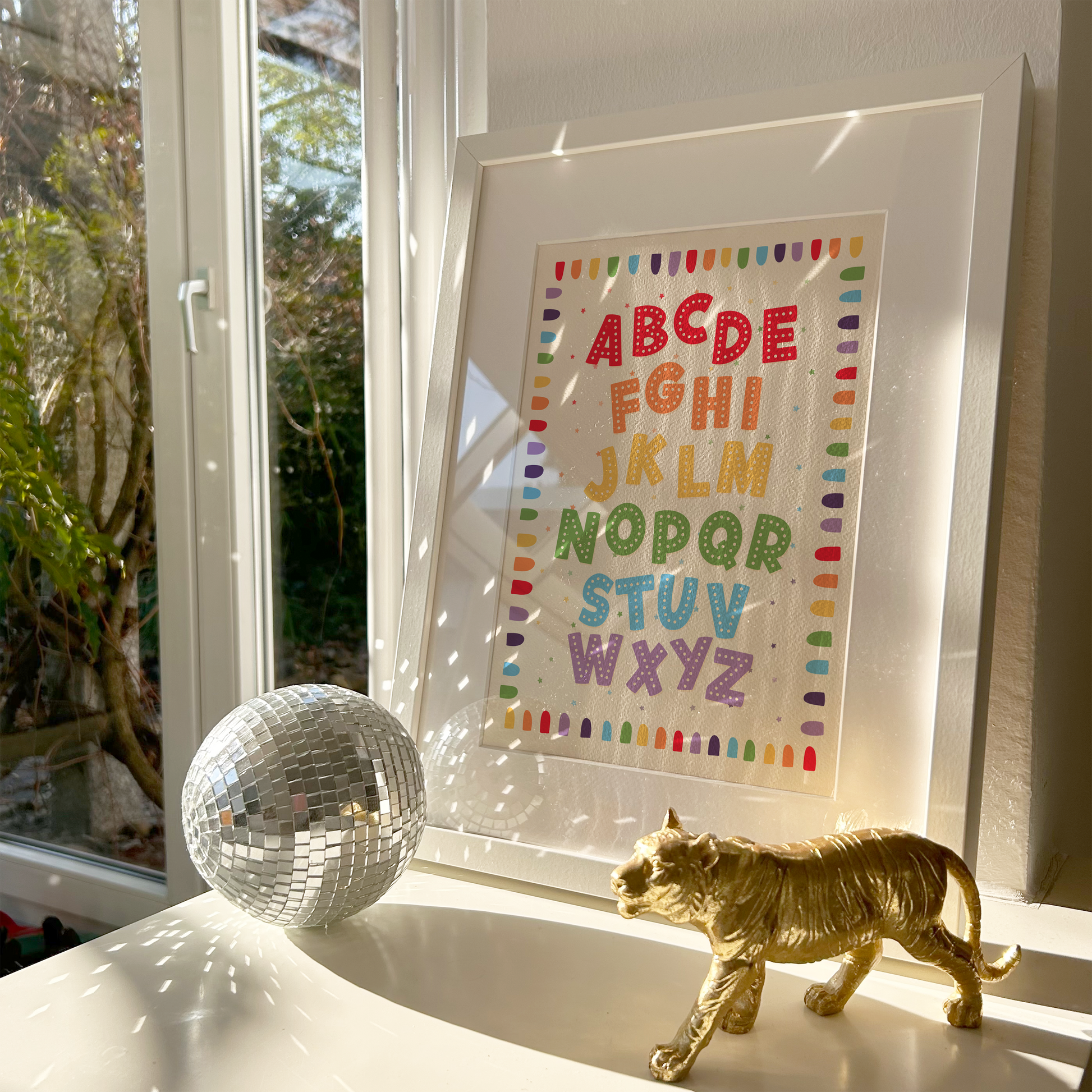 A framed alphabet art print featuring colourful decorative letters A through Z on a cream background, with a decorative border.