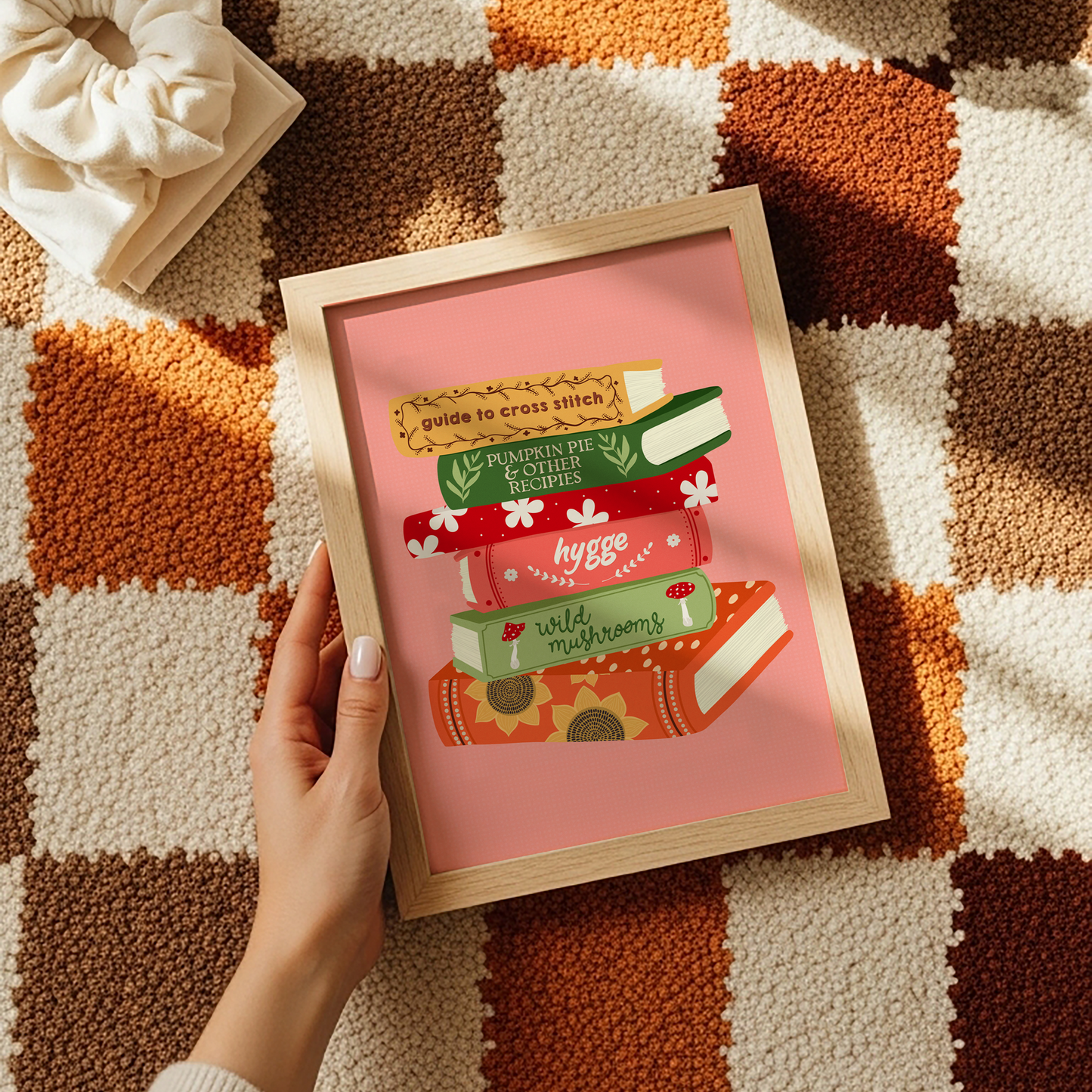 A print featuring six books stacked on top of each other, in autumnal shades and themes on a peachy pink background.