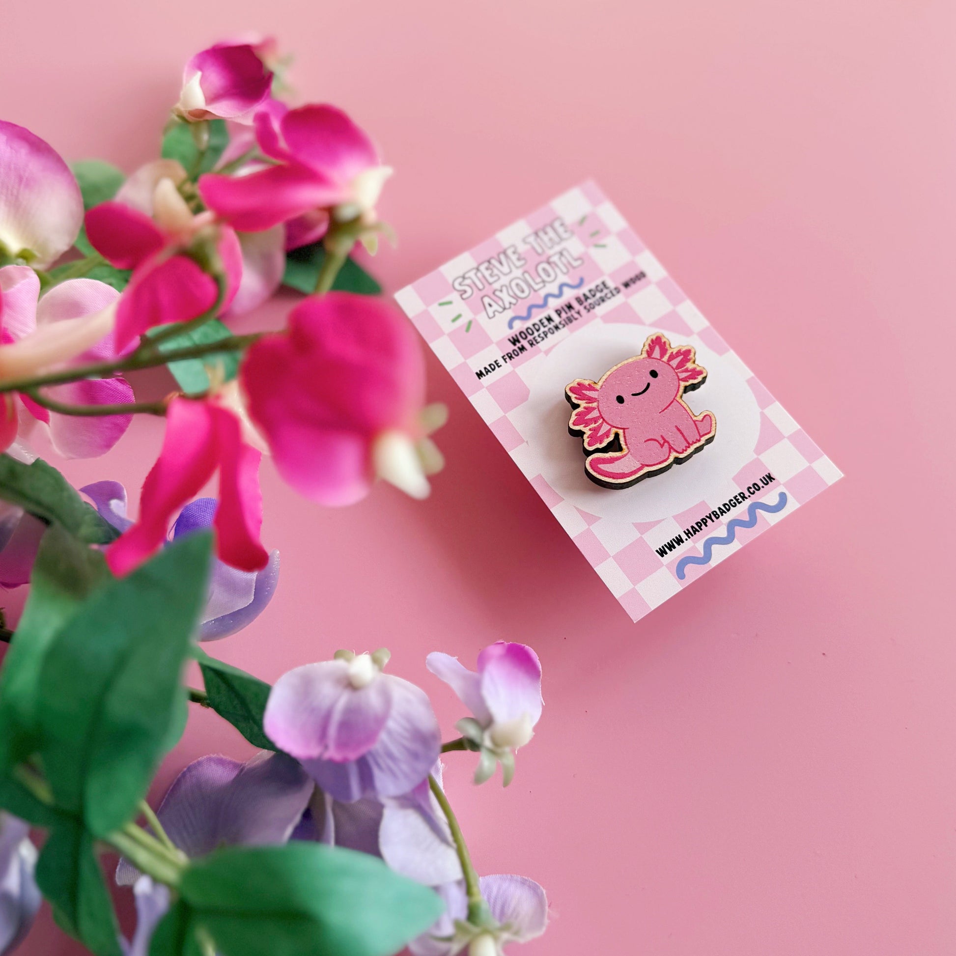 A wooden pin badge with a glossy finish, featuring an illustration of a pink axolotl.