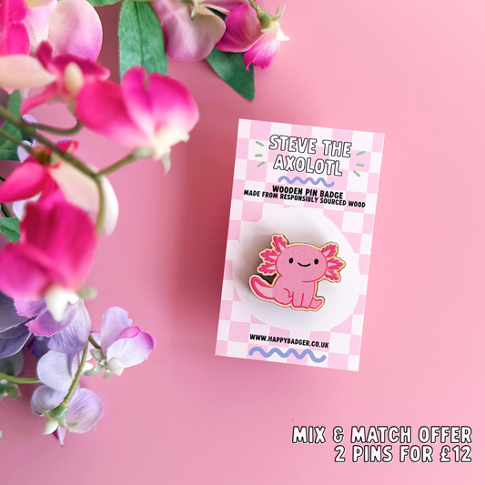 A wooden pin badge with a glossy finish, featuring an illustration of a pink axolotl.