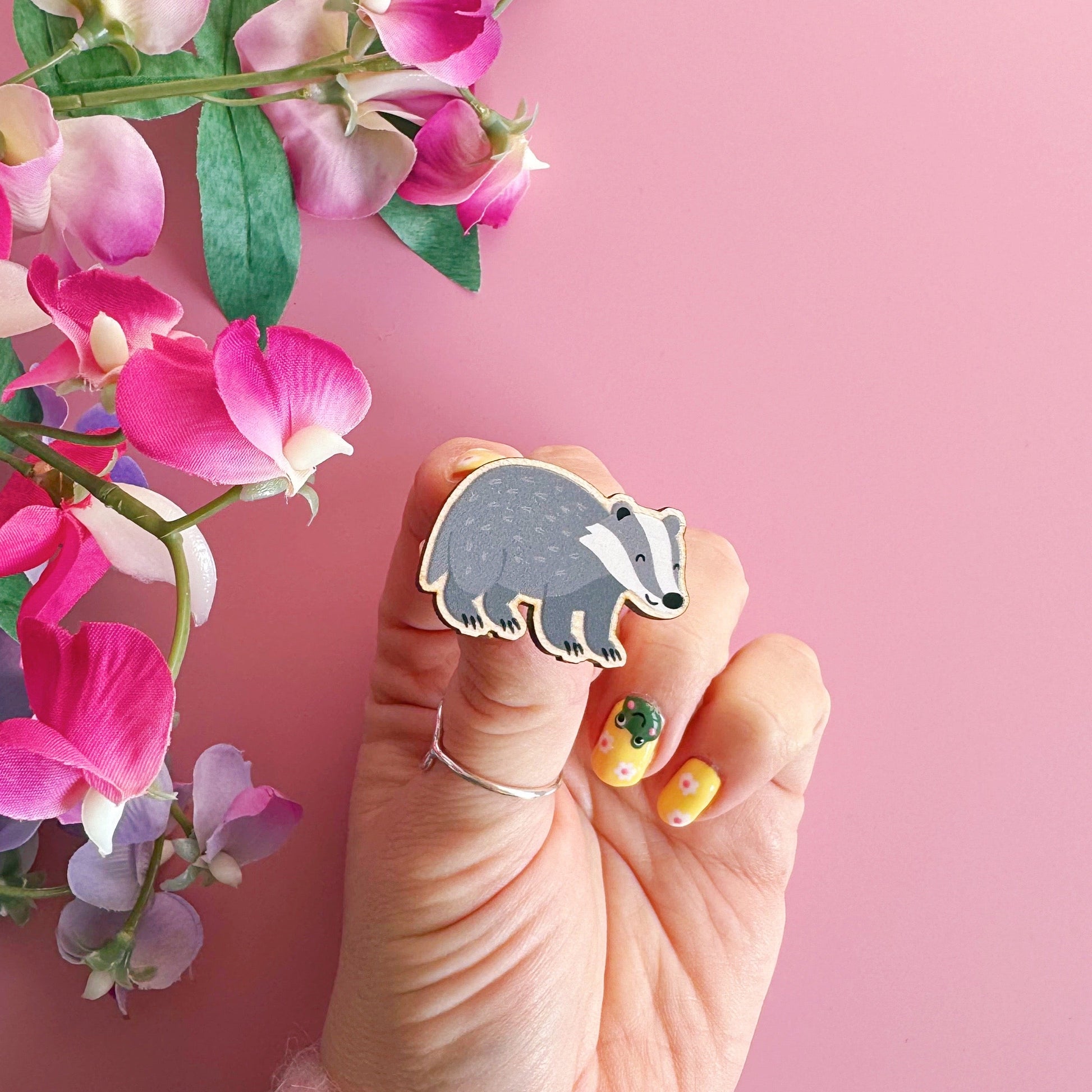 A wooden pin badge with a glossy finish, featuring an illustration of a badger.