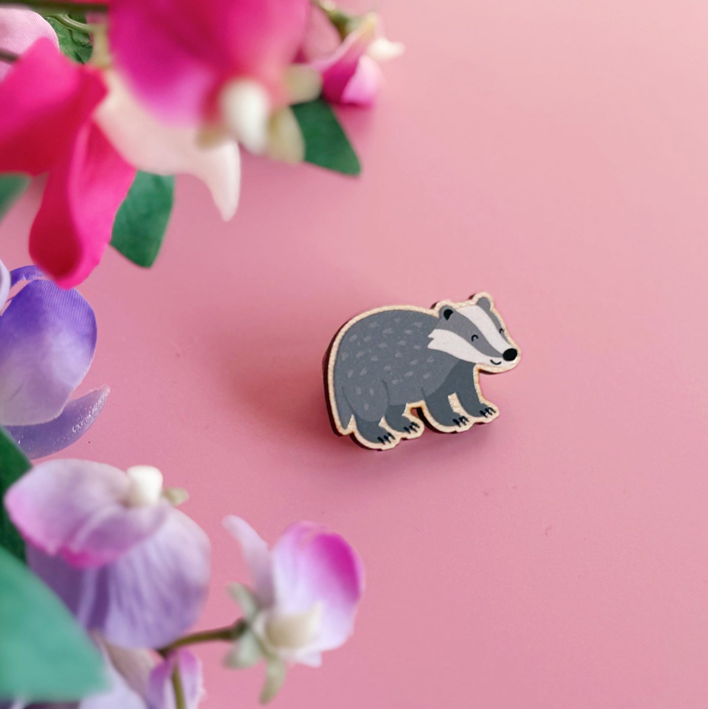 A wooden pin badge with a glossy finish, featuring an illustration of a badger.