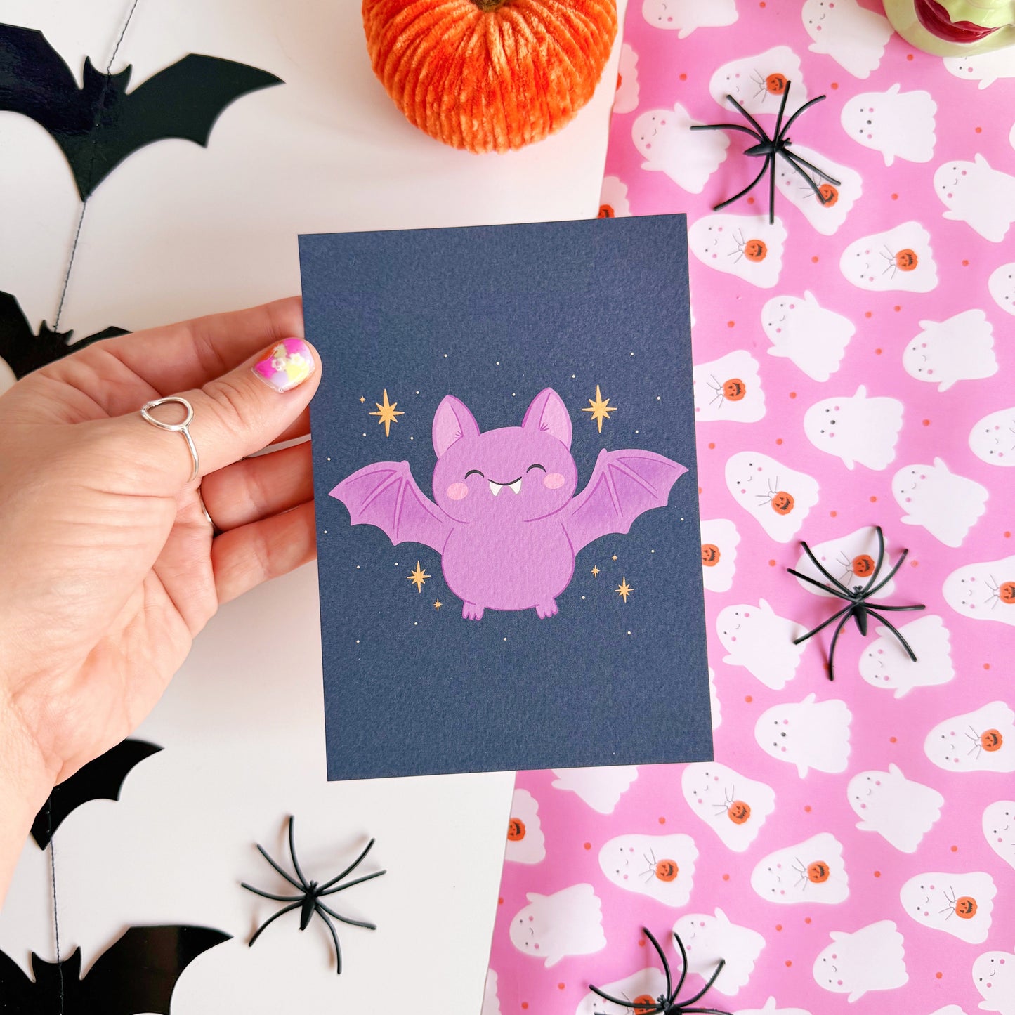 A dark navy postcard with an illustration of a cute looking Halloween bat on the front, with little star doodles around it.