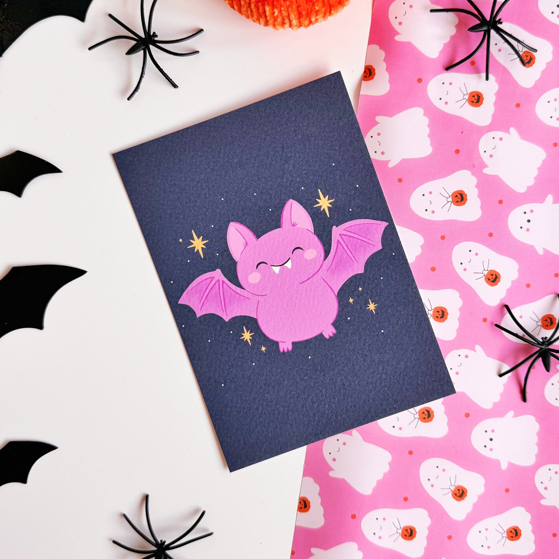 A dark navy postcard with an illustration of a cute looking Halloween bat on the front, with little star doodles around it.