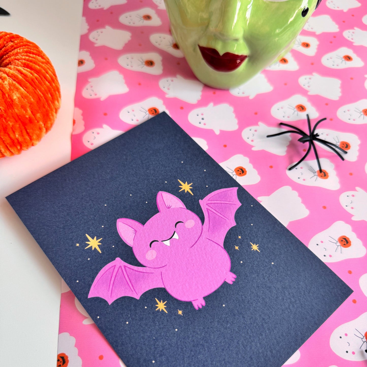 A dark navy postcard with an illustration of a cute looking Halloween bat on the front, with little star doodles around it.